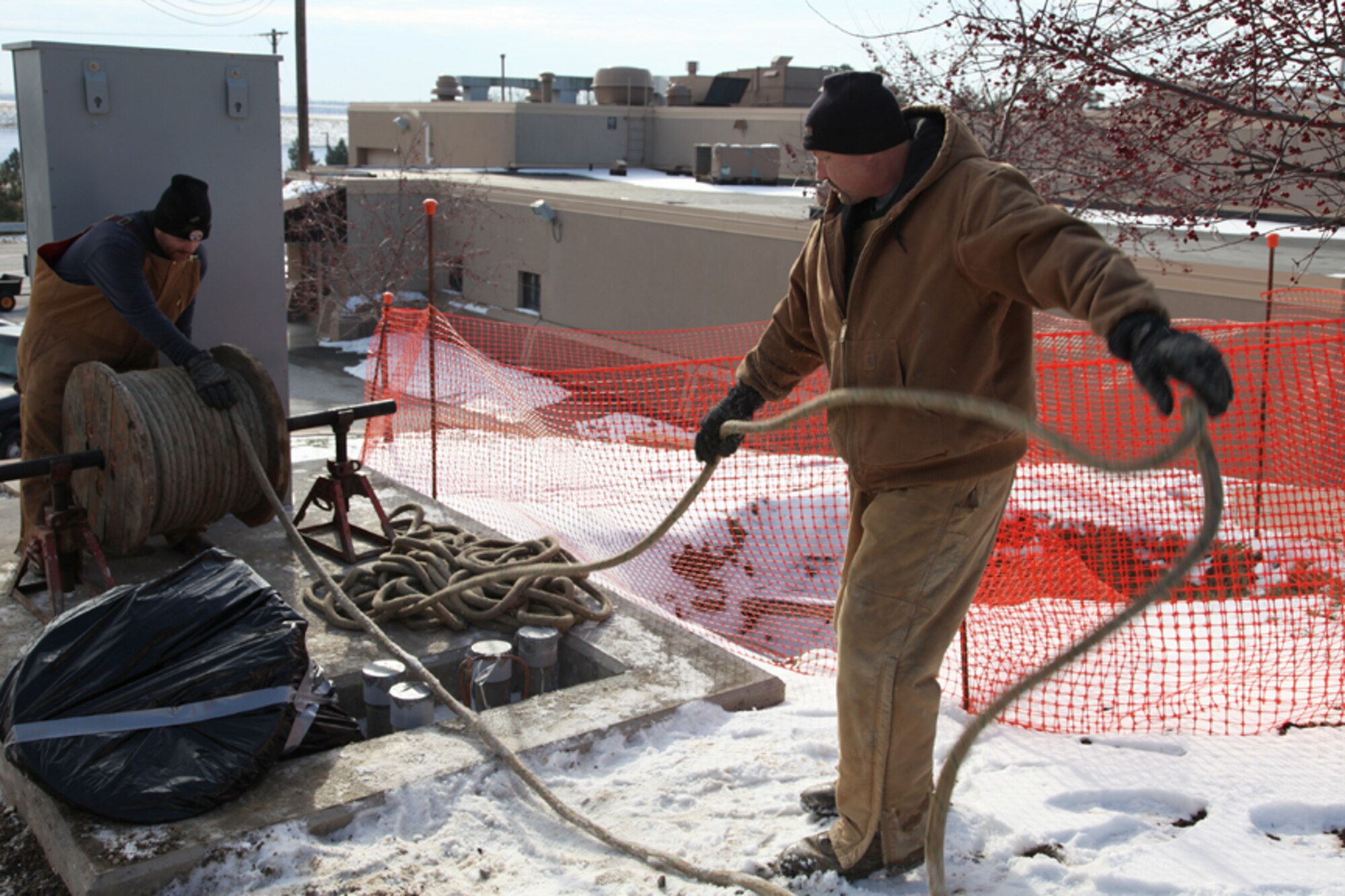 Two civilian contractors reel in a rope used for pulling wire underground, Tuesday, Dec. 21, 2010. Civilian electricians are in the final phase of relocating overhead electrical wires, cables and transformers underground. The high voltage transformers bonded to subversive wiring allow for both separate power control distribution to buildings and lights, and elimination of possible power outages due to inclement weather conditions or accidents. Workers project that the final work will be finished by the end of February 2011.