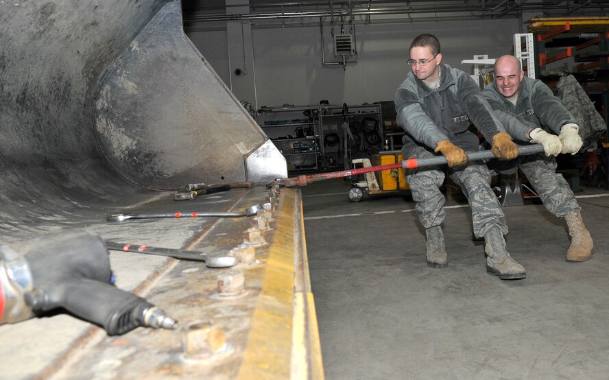 (From left) Airman 1st Class Steven Leary and Tech. Sgt. Christopher Messmer strain on a cheater bar slid over a pipe wrench to loosen rusted bolts on a front-end loader's bucket Dec. 16, 2010, at Misawa Air Base, Japan. The front-end loader is equipped with sacrificial skid plates on the bucket, which take the abuse of grinding on the ground instead of the more expensive bucket. Airman Leary and Sergeant Messmer are 35th Civil Engineer Squadron pavements and equipment construction technicians (U.S. Air Force photo/Tech. Sgt. Phillip Butterfield)