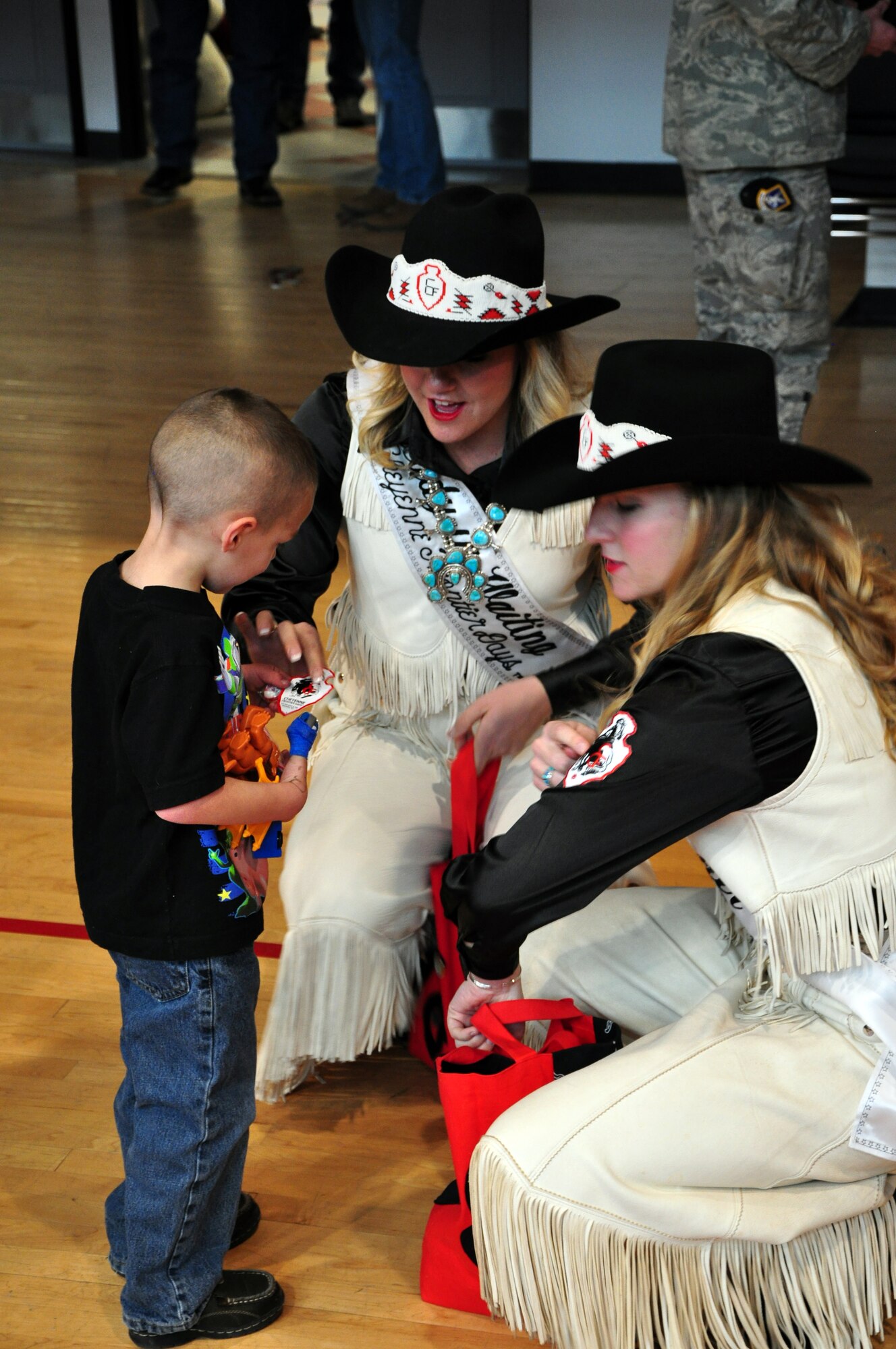 Amy Berry, Miss Frontier, and Sami Jo Heitsch, her Lady-in-Waiting, visit with one of the young children from the Cheyenne community and give him candy and stickers of Cheyenne Frontier Days during Operation Provide Joy, held in the Fall Hall Community Center on Dec. 11. (U.S. Air Force photo by Staff Sgt. Chad Thompson)