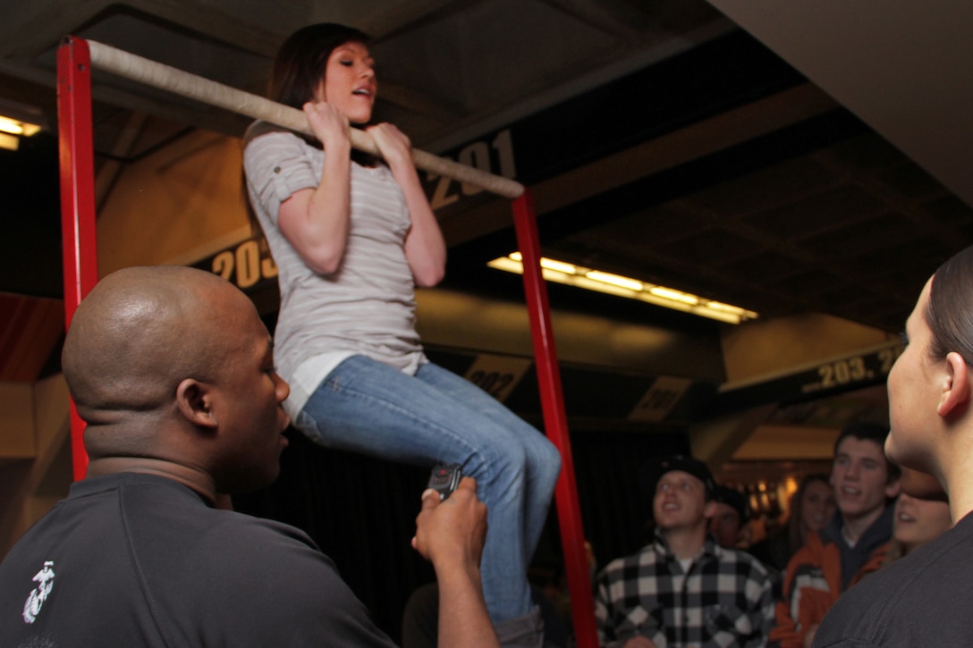 Sgt. Aaron Swan, a 30-year-old recruiter out of Coon Rapids, Minn., starts his stopwatch while Michele Frazer, a 20-year-old attending Brigham Young University, takes the flexed-arm hang challenge at the Target Center Dec. 22 where the Minnesota Timberwolves took on the Utah Jazz. Frazer was the first person who received a Marine Corps T-shirt that night after hanging on the bar for 70 seconds.