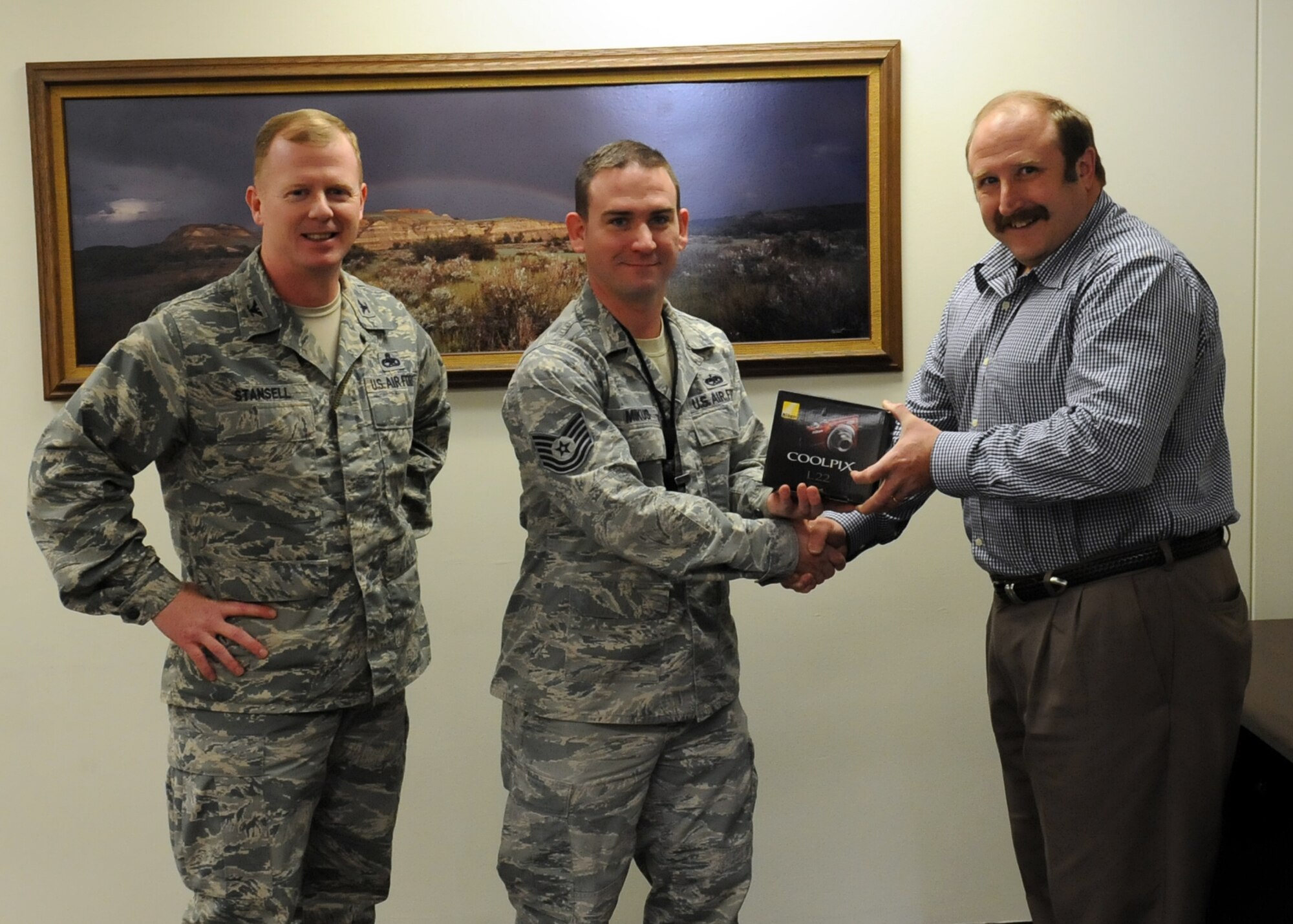 Mr. Mark Kauer, 5th Force Support Squadron manpower management analyst, along with Col. Clifford Stansell, 5th Maintenance Group commander, present a Nikon Coolpix camera to Tech. Sgt. Jamie Mikus, 5th MXG load standardization crew member, as the winner of the Air Force Innovative Development through Employees Awareness program fall promotional give away, here Dec. 21. The IDEA program is an incentive based program designed to solicit ideas that can save the Air Force time and money.(U.S. Air Force photo / Staff Sgt. Keith Ballard)