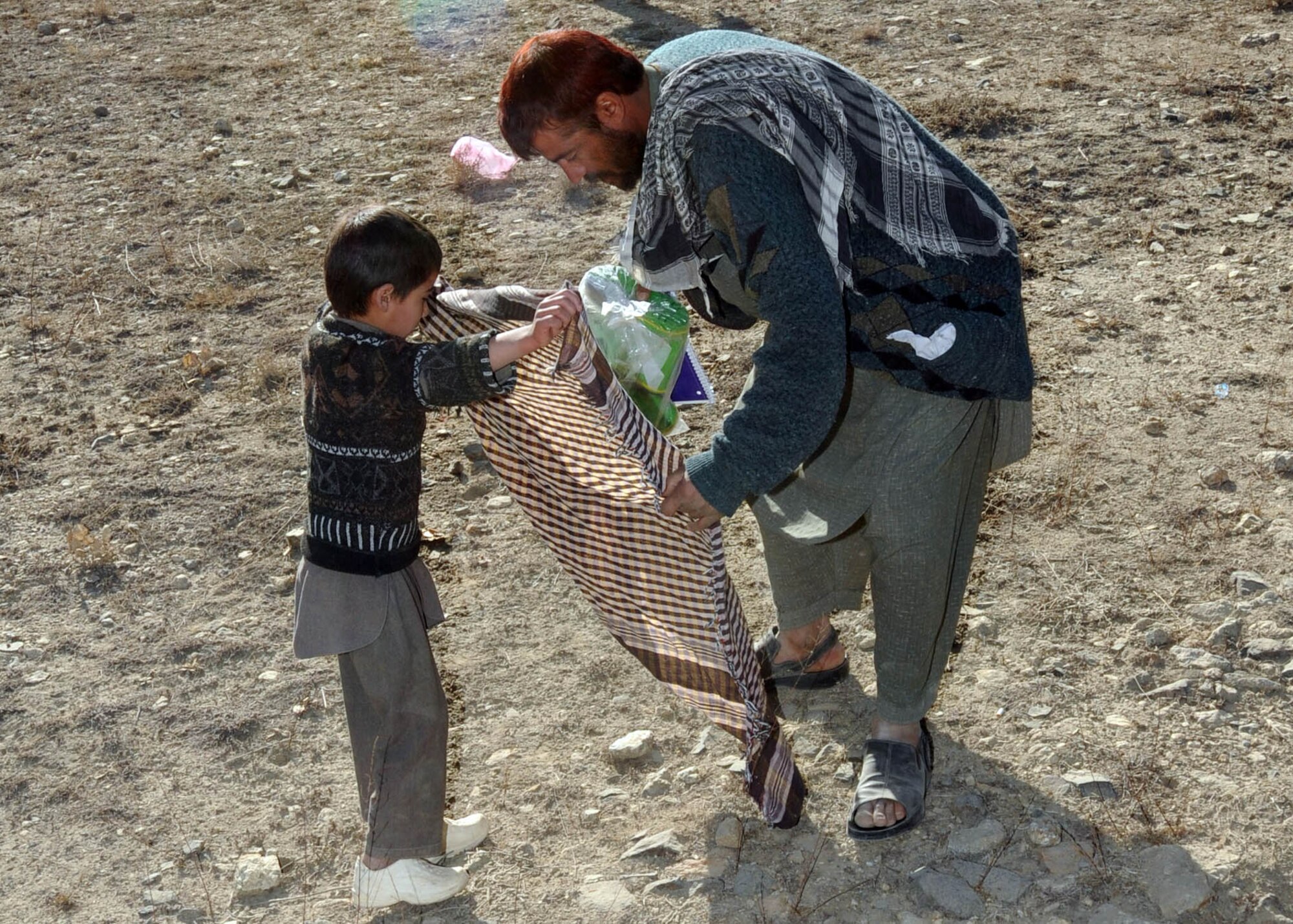 101122-N-6541W-020 KABUL, Afghanistan - A father and son prepare to take their goods home after members of the Afghan Air Force  distribute supplies to children and their families in a village north of Kabul.  (U.S. Navy photo by Mass Communication Specialist 3rd Class Jared Walker/ RELEASED).