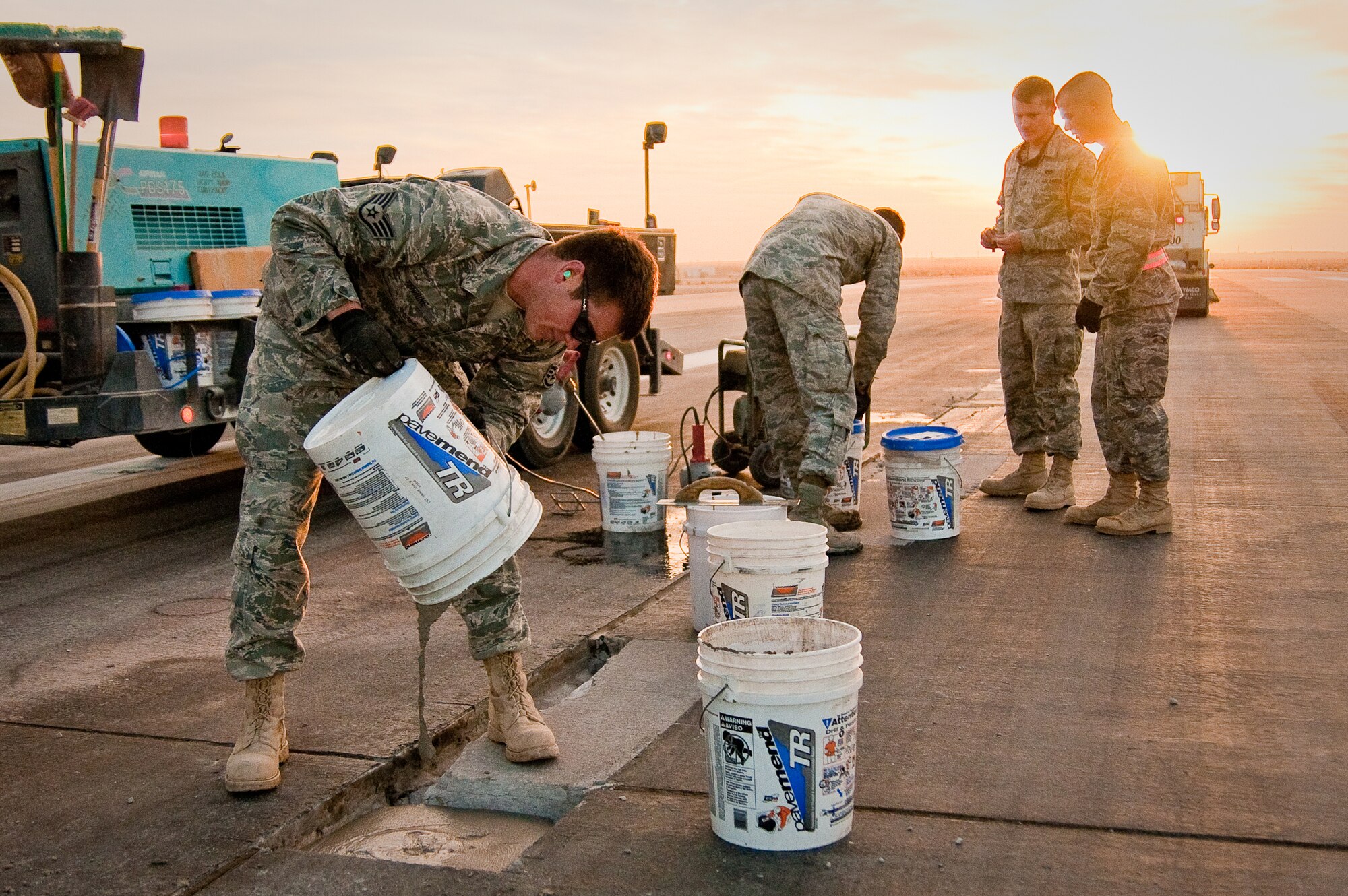 SOUTHWEST ASIA - Staff Sgt. Brandon Terhune (left) of the 386th Expeditionary Civil Engineer Squadron pours fresh mortar into an excavated cavity on one of the runways at an undisclosed air base here Dec. 10, 2010, while other members of the squadron's Runway Repair Team prepare additional mortar. The team makes weekly repairs to prevent aircraft from being damaged by foreign object debris. (U.S. Air Force photo by Maj. Dale Greer)