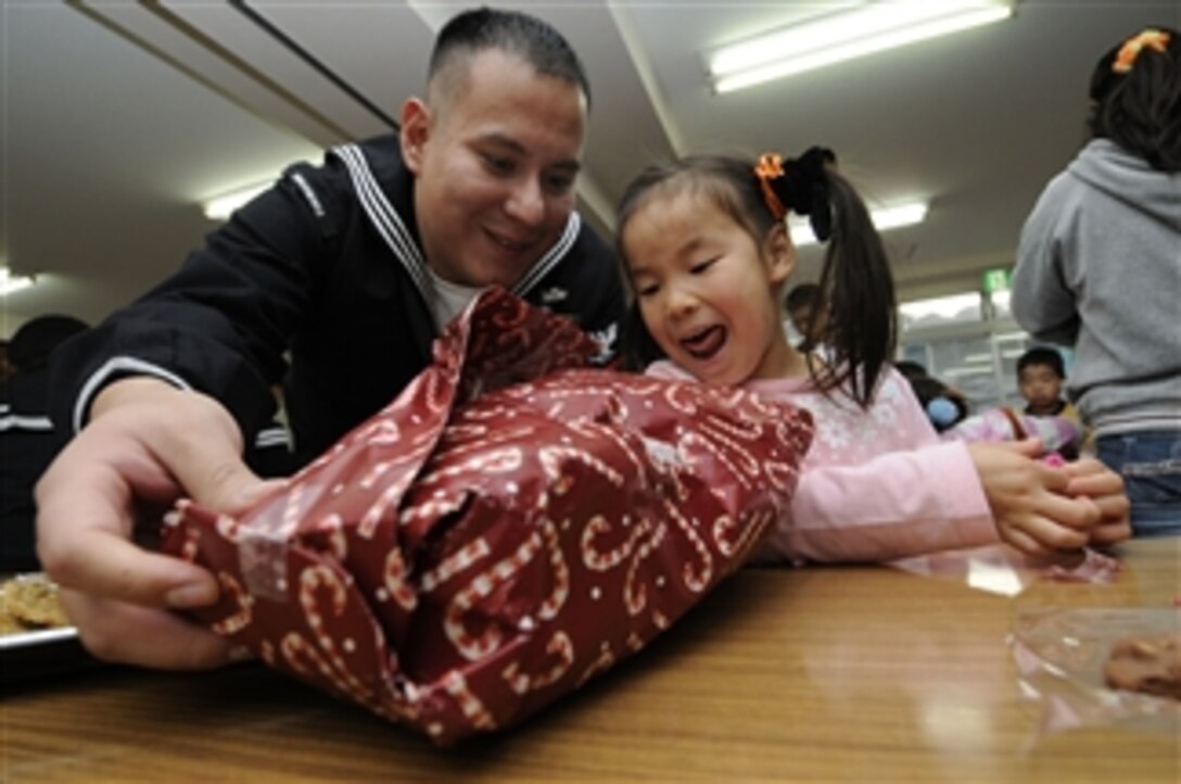 U.S. Navy Petty Officer 1st Class Oscar Bernuy (left), with the 7th Fleet, helps an orphan open her gift at the Shunko Gakuen Boys and Girls Home at Yokosuka, Japan, on Dec. 22, 2010.  