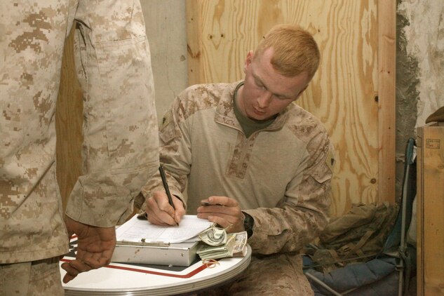 Cpl. Alex P. Jones, disbursing clerk, Headquarters and Service Company, 1st Marine Logistics Group (Forward), issues casual pay to a Marine with 1st Battalion, 10th Marine Regiment, 1st Marine Division (Forward) near the Kajaki Dam, Dec. 25, in order to purchase items from the "mobile PX." Marines with Marine Corps Community Services arrived in Kajaki on Christmas day to provide goods such as snacks and other comfort items to the Marines in the area.
