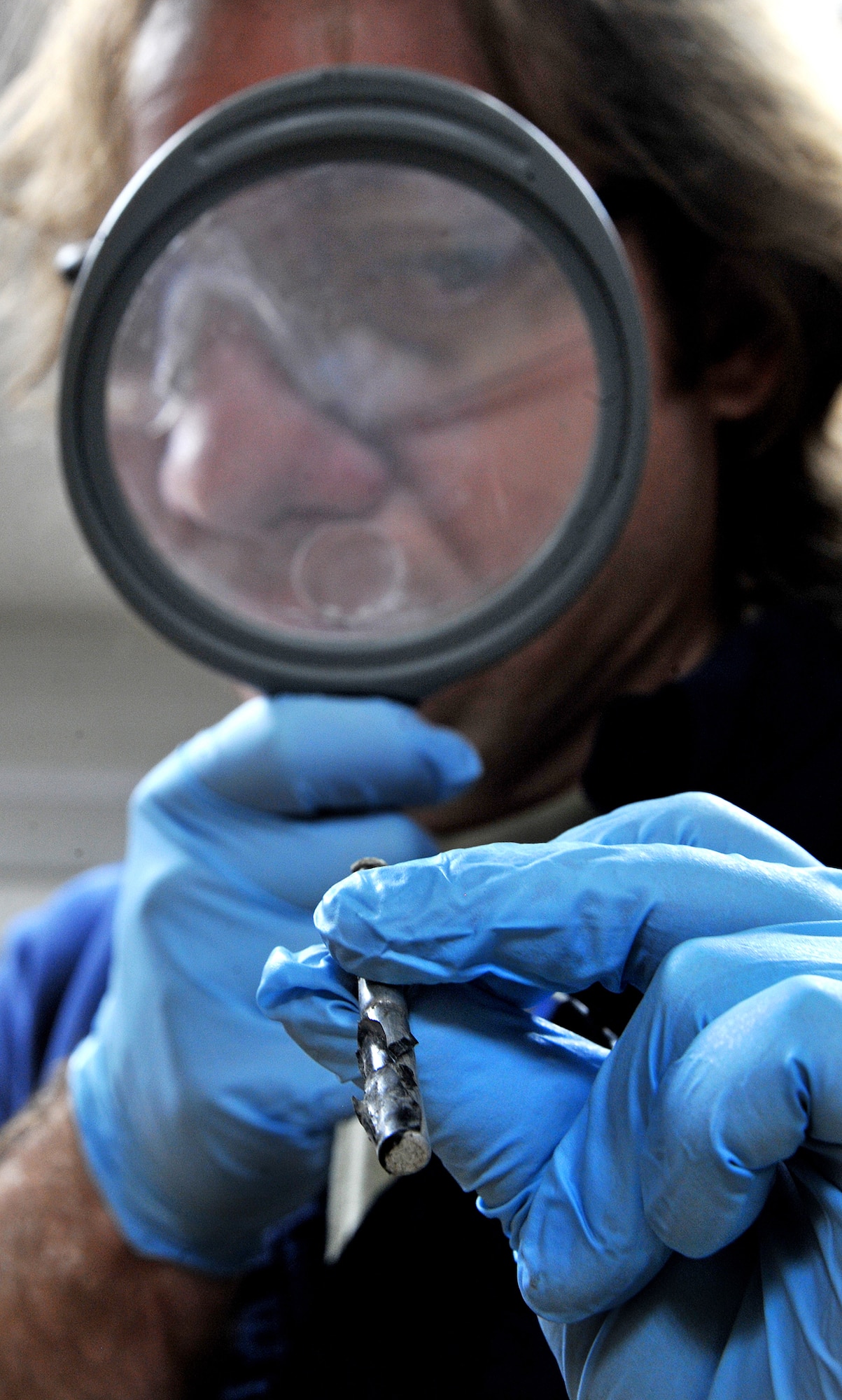 Phil Whitley, an explosives enforcement officer with the Bureau of Alcohol, Tobacco, Firearms and Explosives and member of United States Forces-Iraq Combined Joint Task Force Troy’s Combined Explosives Exploitation Cell, takes a closer look through a magnifying glass at a piece from an improvised explosive device to search for any identifying marks Dec. 8, 2010, on Camp Victory, Iraq. One key responsibility of CJTF Troy and CEXC is neutralizing the improvised explosive devices’ threat through collection and exploitation of IED evidence and related intelligence. CJTF Troy is dedicated to countering IEDs and saving lives of Iraqi and joint forces conducting Operation New Dawn. (U.S. Air Force photo by Senior Airman Andrew Lee)