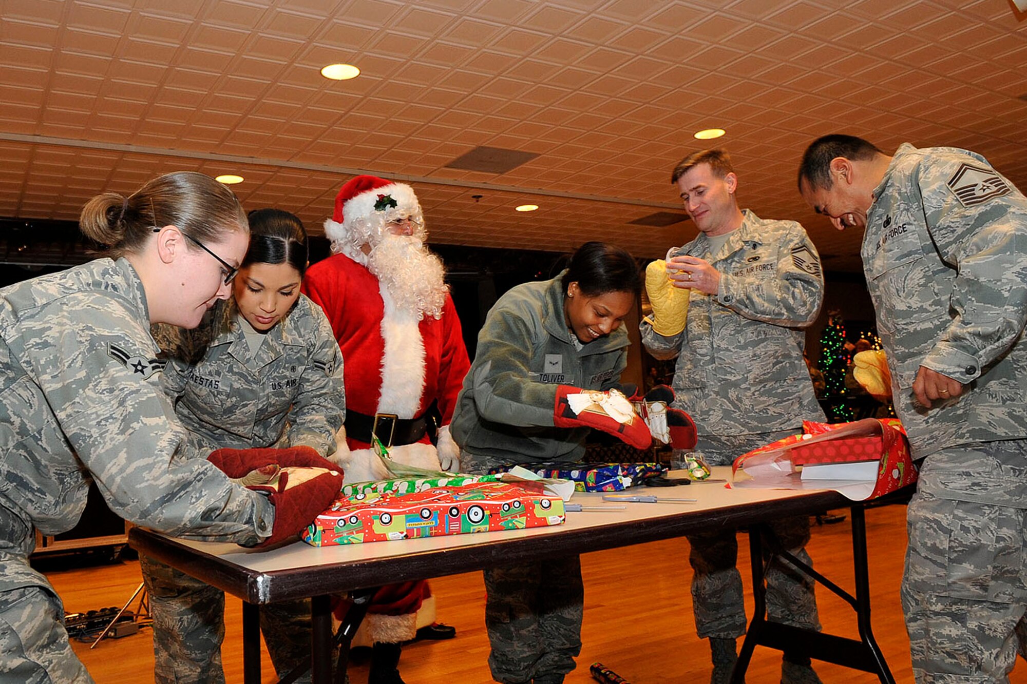 PETERSON AIR FORCE BASE, Colo. – Santa Claus judges a holiday competition as Airmen try their luck wrapping Christmas presents while wearing oven mitts during the 21st Space Wing Holiday Party Dec 17 at The Club. Airman 1st Class Vanessa Toliver (center), 21st Operations Group, won the contest. More than 250 Airmen and civilians enjoyed food, door prizes, games and music by the U.S. Air Force Academy “Blue Steele” band during the annual holiday celebration. (U.S. Air Force photo/Rob L. Bussard)