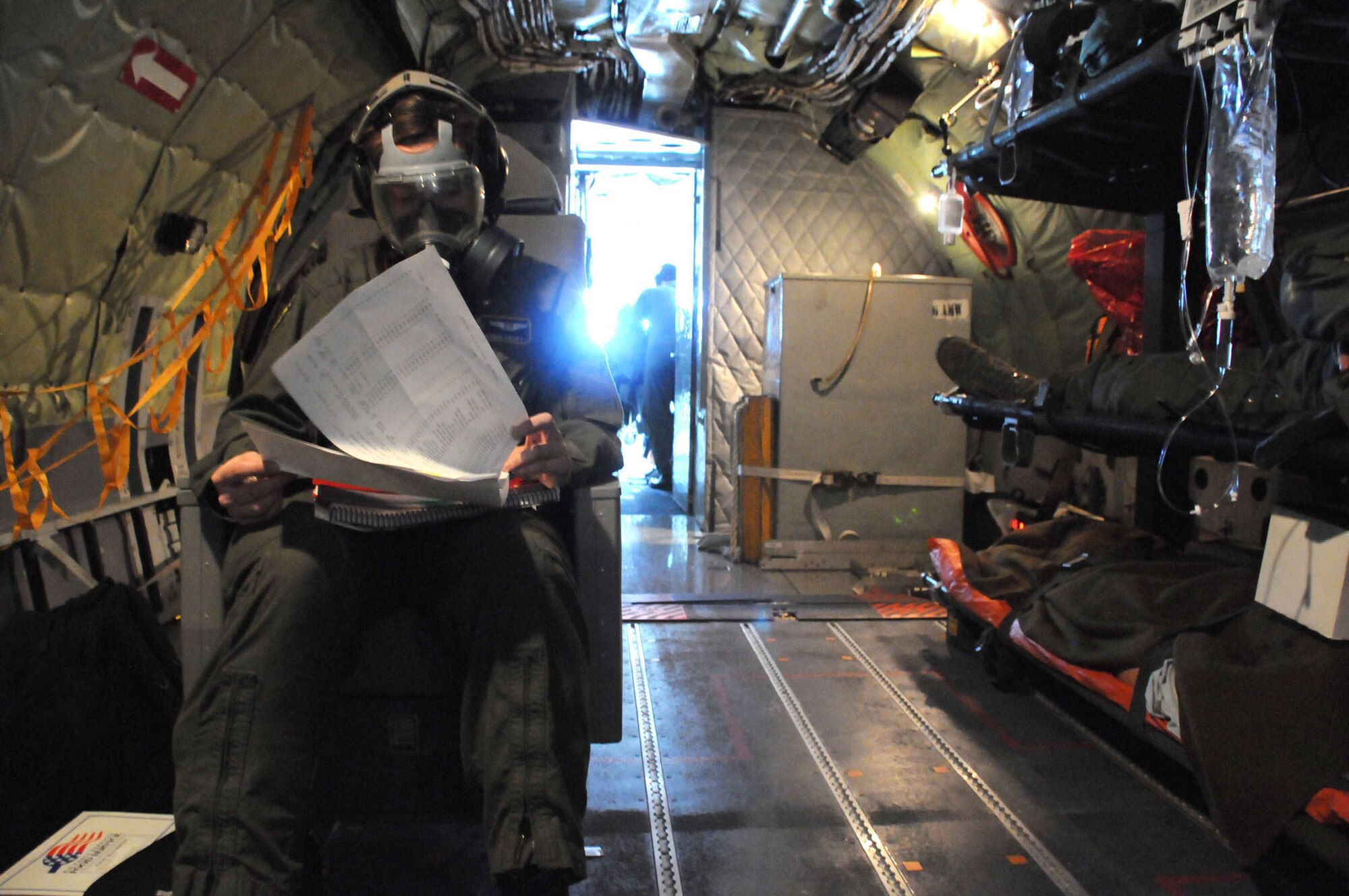 MacDill Air Force Base, Fla. -- Senior Airman Robin Croft, a flight medic with the 63rd Aeromedical Evacuation Squadron, reviews paperwork while a teammate-patient sleeps nearby.  Croft is training with her unit to prepare to handle real-world patients, many of whom will come from combat zones.  As part of the training, the Plant City, Fla. native is required to spend time in her gas mask.  All flight medical personnel have to be qualified to do their jobs in a chemical, biological, or nuclear-attack setting.  (Official U.S. Air Force photo by Staff Sgt. Shawn Rhodes)
