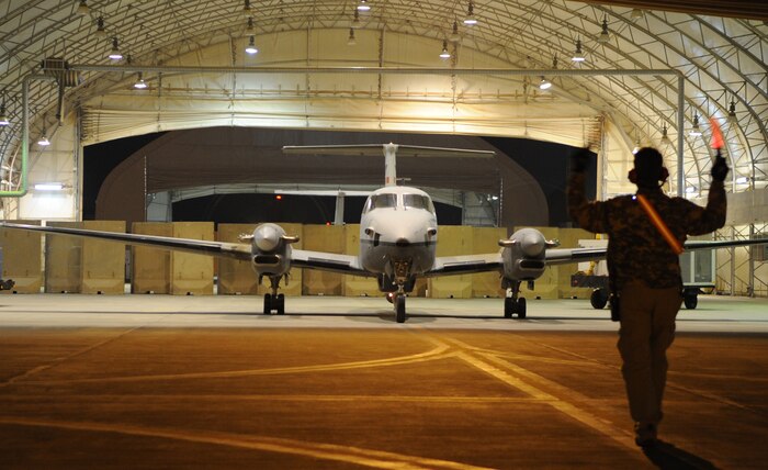 JOINT BASE BALAD, Iraq -- A contract field service technician, guides an MC-12 out of a hangar Dec. 30, 2010. The aircraft is on its way to execute the 362nd Expeditionary Reconnaissance Squadron’s 5,000th sortie in just 18 months. (U.S. Air Force photo/ Staff Sgt. Keyonna Fennell)