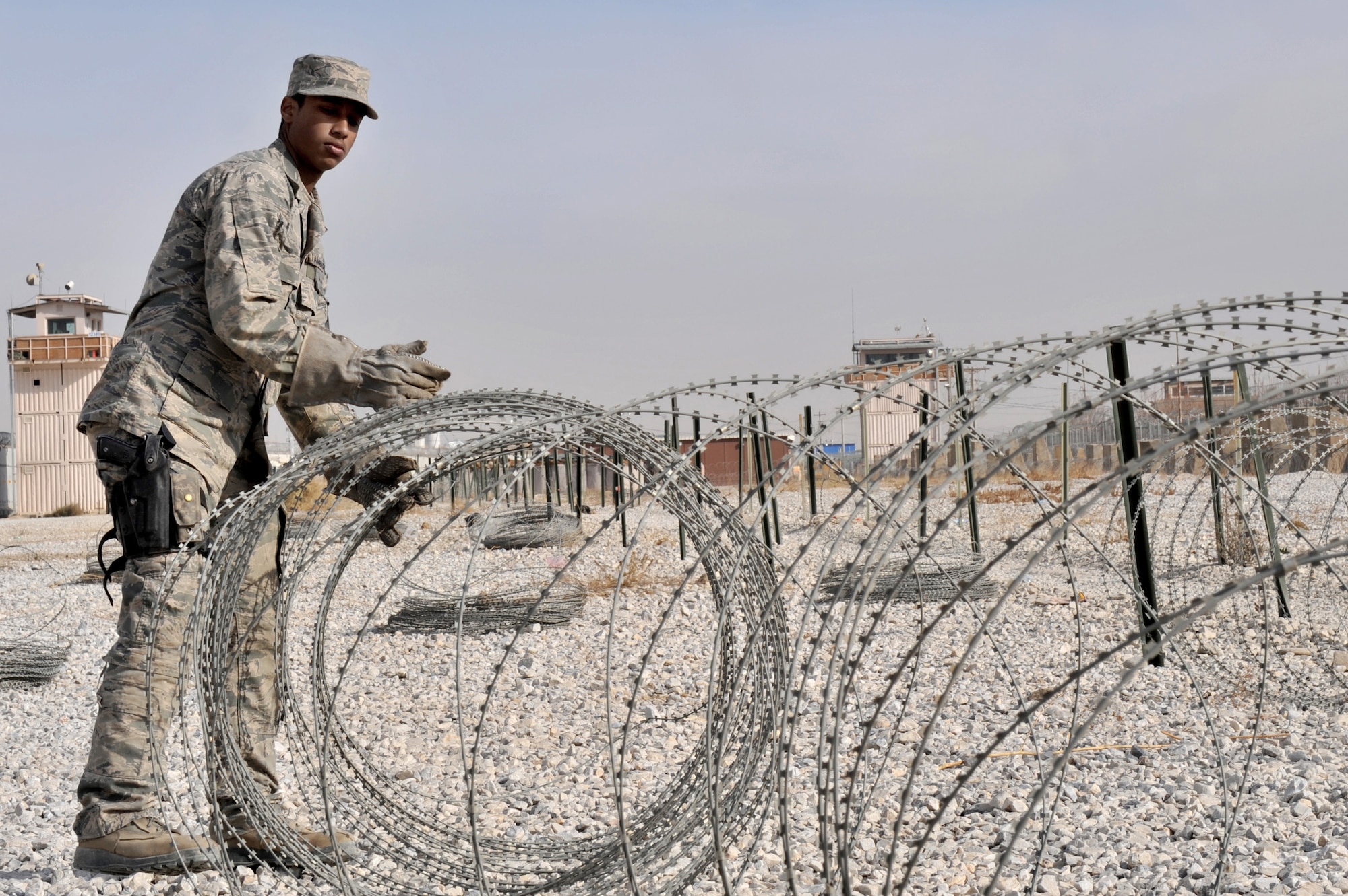 Airman 1st Class Lee Tamburro, 455th Expeditionary Security Forces Squadron, moves concertina wire lay out on the gravel to the walking path pavement, Bagram Airfield, Afghanistan, Dec. 30, 2010. The security forces airman are moving the C-wire from the gravel to a pavement walking path which local national employee use every day. The move of the C-wire is to improve the quality of life for the more than five thousand Bagram local national employees. (Air Force photo/Senior Airman Sheila deVera)