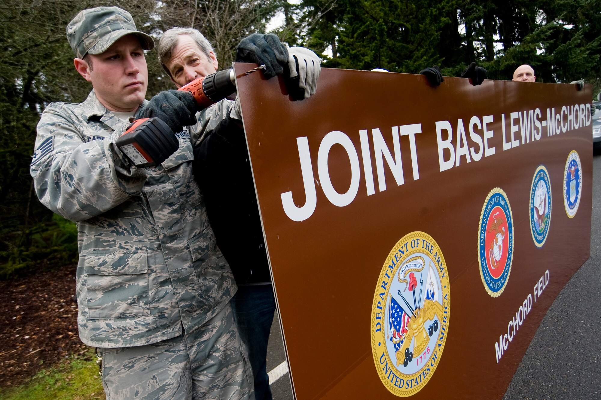 Staff Sgt. Jeffery Cardinal, left, and Craig Hayes, 62nd Civil Engineer Squadron, drill holes in the new Joint Base Lewis-McChord sign at the main gate Sunday in preparation of Initial Operational Capability of Joint Base Lewis-McChord. (U.S. Air Force Photo/Abner Guzman)