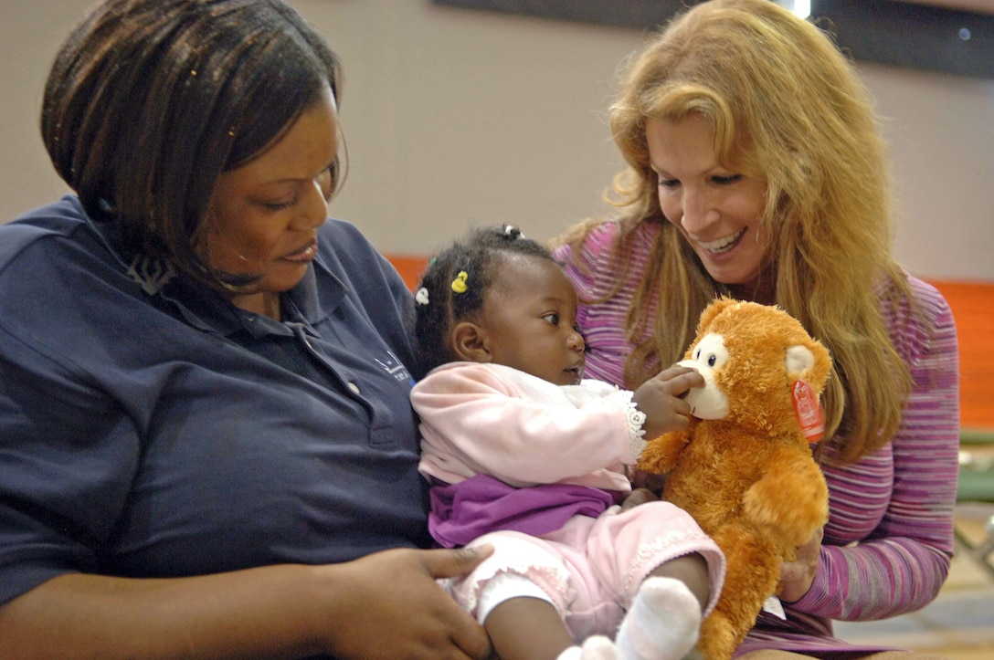 Francis Dugue (left) holds 6-month-old evacuee Anaellen Jean Louis as she plays with a teddy bear donated by Michele Gillen Jan. 24, 2010, at Homestead Air Reserve Base, Fla. Mrs. Gillen donated 2,500 of the bears to children of displaced evacuees at Homestead ARB and other places in the Miami area on behalf of Bear Hugs for Haiti. Mr. Dugue is a Miami-Dade 311 government center Memployee. Mrs. Gillen is an an WFOR-TV Miami chief investigative reporter. (U.S. Air Force photo/Tech. Sgt. Andy Bellamy) 