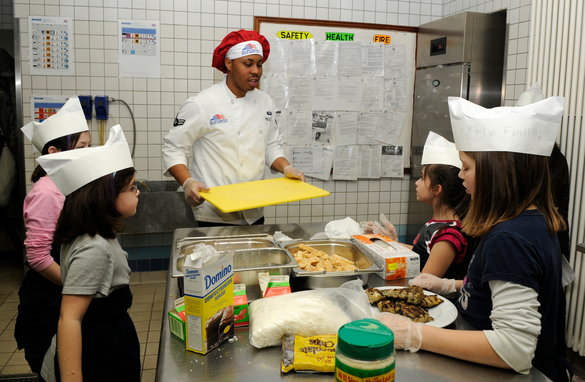 SPANGDAHLEM AIR BASE, Germany –Airman 1st Class Adrian Paisley, 52nd Force Support Squadron, helps various teams on the cutting board during the Kid’s Iron Chef Competition at the Mosel Dining Facility Jan. 27. Students from the Spangdahlem Middle School were split into three teams, and each team created a different dish to be judged. Team Three took first place with their sweet chicken curry dish.  (U.S. Air Force photo/Airman 1st Class Staci Miller)