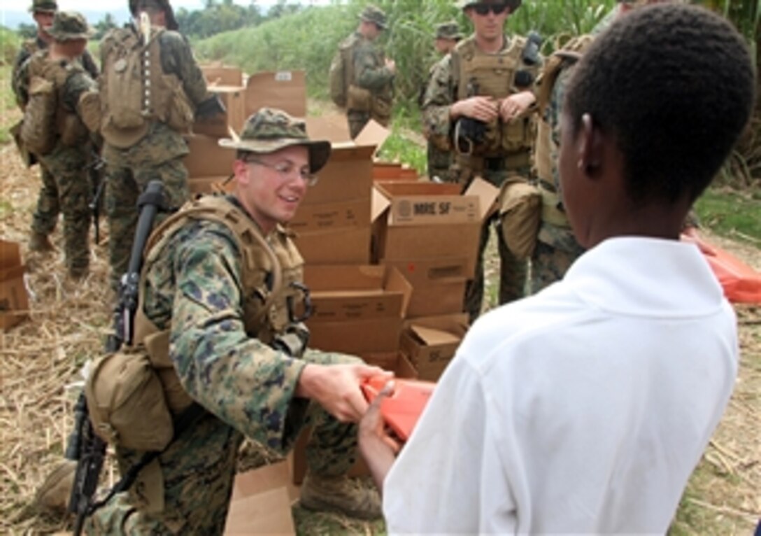 A U.S. Marine with Battalion Landing Team, 3rd Battalion, 2nd Marine Regiment hands rations to a Haitian earthquake victim near Leogane, Haiti, on Jan. 26, 2010.  Marines flew into the area two days ago to establish a humanitarian aid distribution site.  