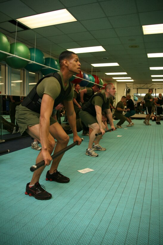 Marines perform squats with a weighted bar during a semper fit class at Cherry Point's Fitness Connection, Feb. 2. According to Vicky Lee, the fitness program coordinator for the semper fit program, this class in particular is geared toward preparing Marines for the combat fitness test, a yearly analysis of a devil dog’s ability to withstand the physical rigors of combat.