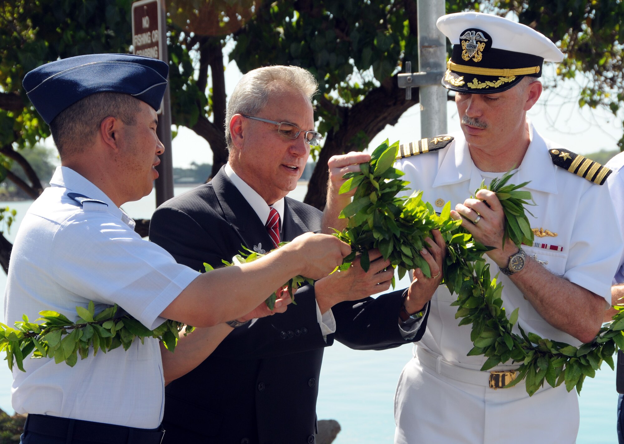 JOINT BASE PEARL HARBOR HICKAM, Hawaii -- U.S. Air Force Col. Giovanni Tuck, 15th Airlift Wing commander, Pastor Ed Sproat and U.S. Navy Capt. Richard Kitchens, Joint Base Pearl HArbor Hickam commander, symbolically join a  traditional Hawaiian lei Jan. 31 during a ceremony marking the official initial operational capability transition combining capabilities from Hickam and Pearl Harbor installations. The transition will continue to Oct. 1 when full operational capabilities will be achieved. At that time, all resources, property, personnel and authority for installation management functions will transfer to the Navy, which was designated by the 2005 BRAC law to be the lead agency for the new installation.  