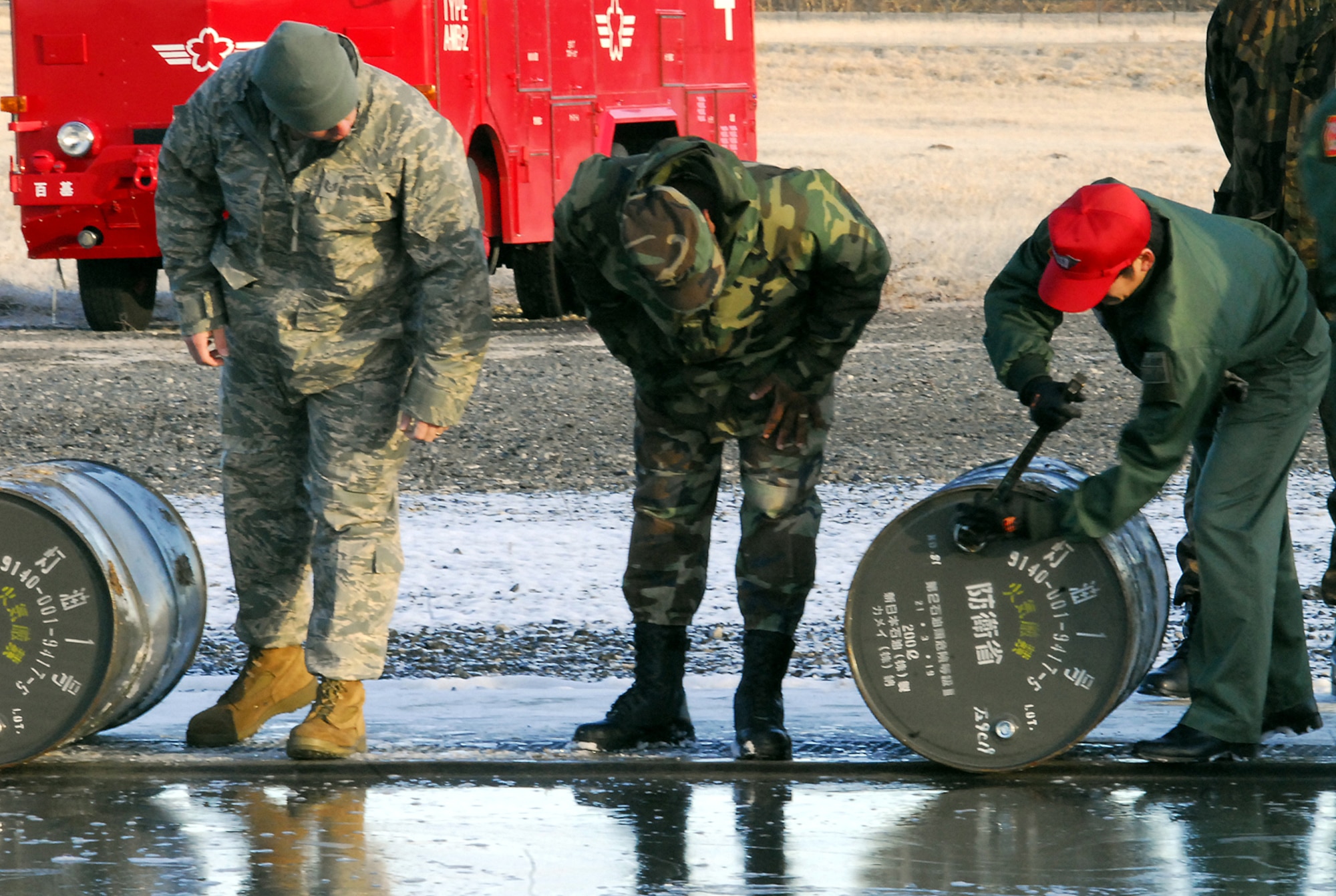 Tech. Sgt. Daniel Morris (left) and Staff Sgt. Davie Hobbs, firefighters from the 18th Civil Engineer Squadron, watch as a Japan Air Self Defense Force firefighter loosens the cap on a drum of fuel for a controlled burn Feb. 3 at Hyakuri Air Base, Japan. (U.S. Air Force photo / 1st Lt. Bryan Bouchard)
