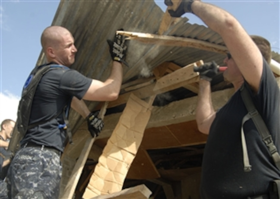 U.S. Navy Petty Officer 2nd Class David Larson and Senior Chief Petty Officer Jeremy Fleming repair a damaged roof on a building on Gonave Island, Haiti, on Jan. 27, 2010.  The sailors, from the amphibious dock landing ship USS Fort McHenry (LSD 43), are participating in Operation Unified Response.  They are providing military support to civil authorities to help stabilize and improve the situation in the island nation.  