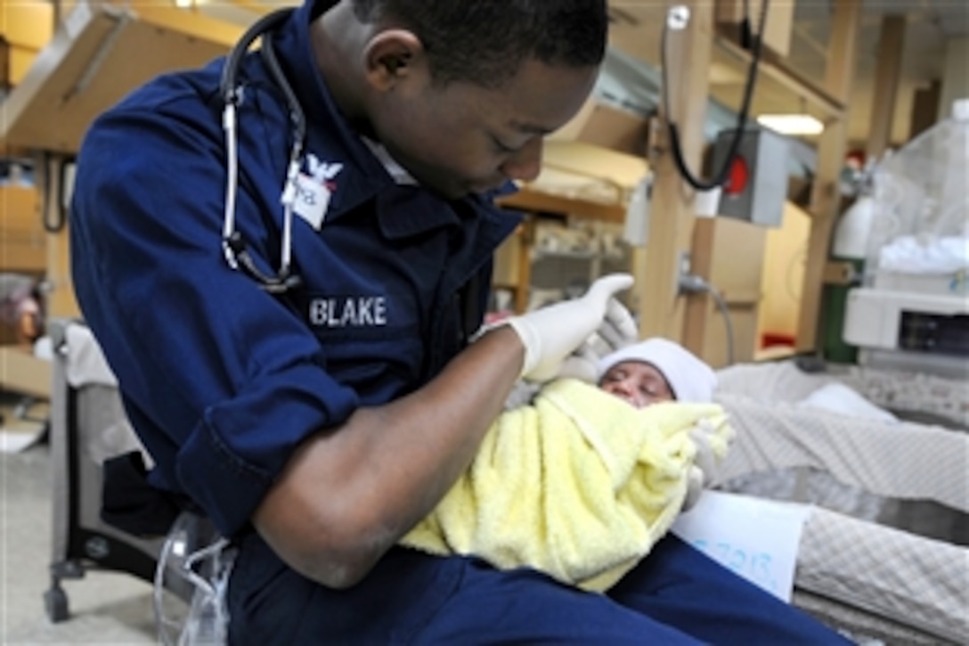 U.S. Navy Petty Officer 3rd Class Matthew Blake holds a newborn baby aboard the USNS Comfort in Port-au-Prince, Haiti, Jan. 28, 2010. Blake assisted in resuscitating the baby moments after it was born earlier in the week. The Comfort is participating in Operation Unified Response, providing medical care to Haiti earthquake victims.
