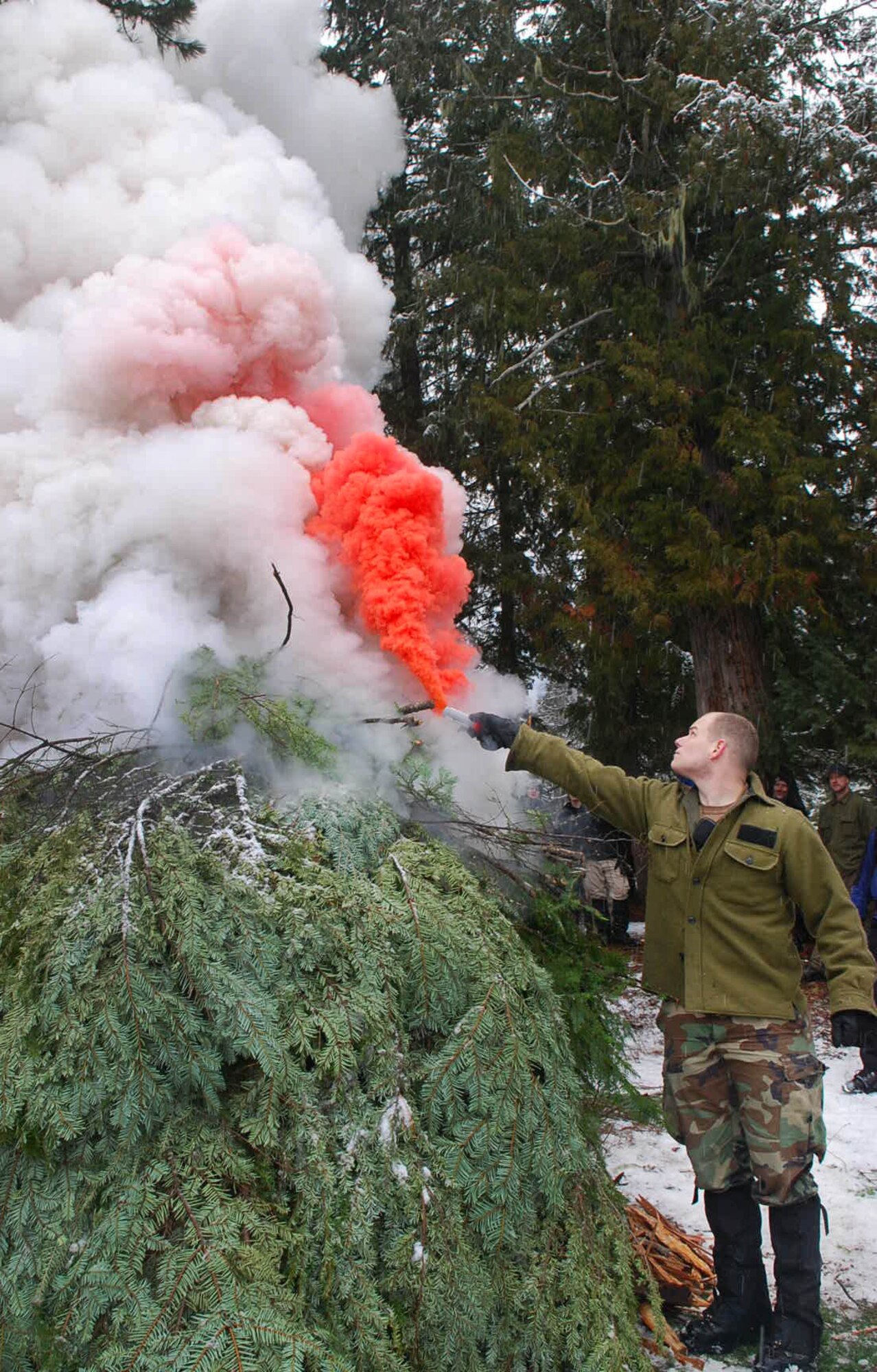 PRIEST LAKE, Idaho - Senior Airman Jonathan Case, SERE Specialist, holds an orange smoke flare to a smoke generator during the winter survival training at Priest Lake. (U.S. Air Force photo / Senior Airman Emerald Ralston)