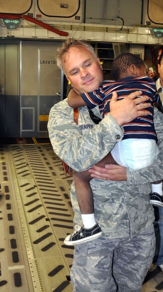 Lt. Col. Randon Draper, of the 621st Contingency Response Wing, carries a weary Haitian orphan aboard an Air Force Reserve C-17 aircraft Jan. 22. The aircraft transported the boy – and 22 other orphans – to Orlando, Fla., where the children were united with their new adoptive parents. (U.S. Air Force photo/Bryan Magaña)