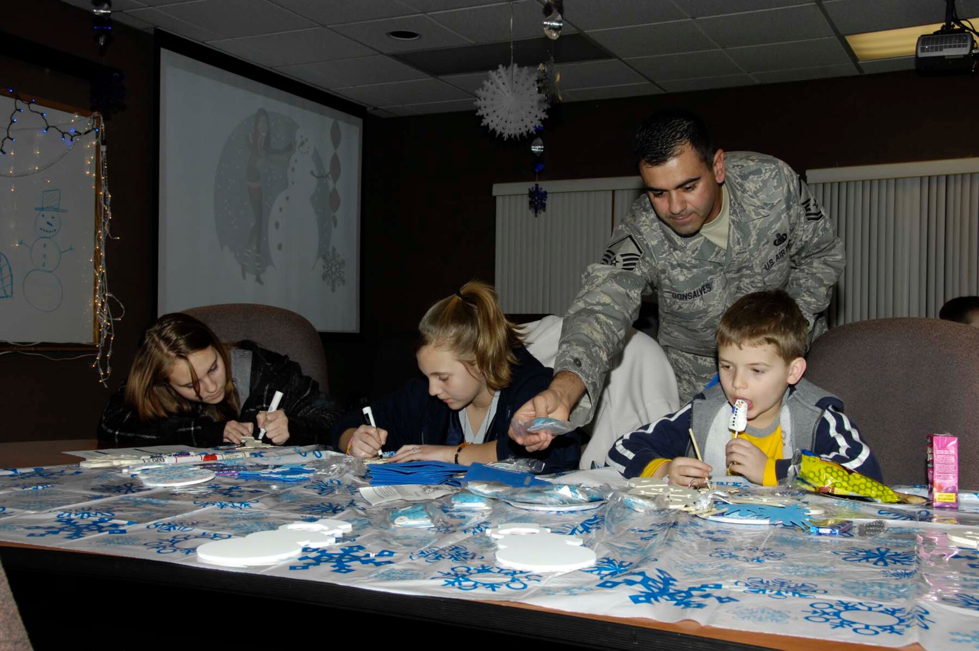 Master Sgt. Don Gonsalves, family readiness coordinator with the 66th Force Support Squadron lends a helping hand to (from l to r) Alyssa, Meghan and Christian Cattles  as they work on the Hearts Apart Winter Wonderland art project at the Airman Family and Readiness Center. (U.S. Air Force photo by Linda LaBonte-Britt) 