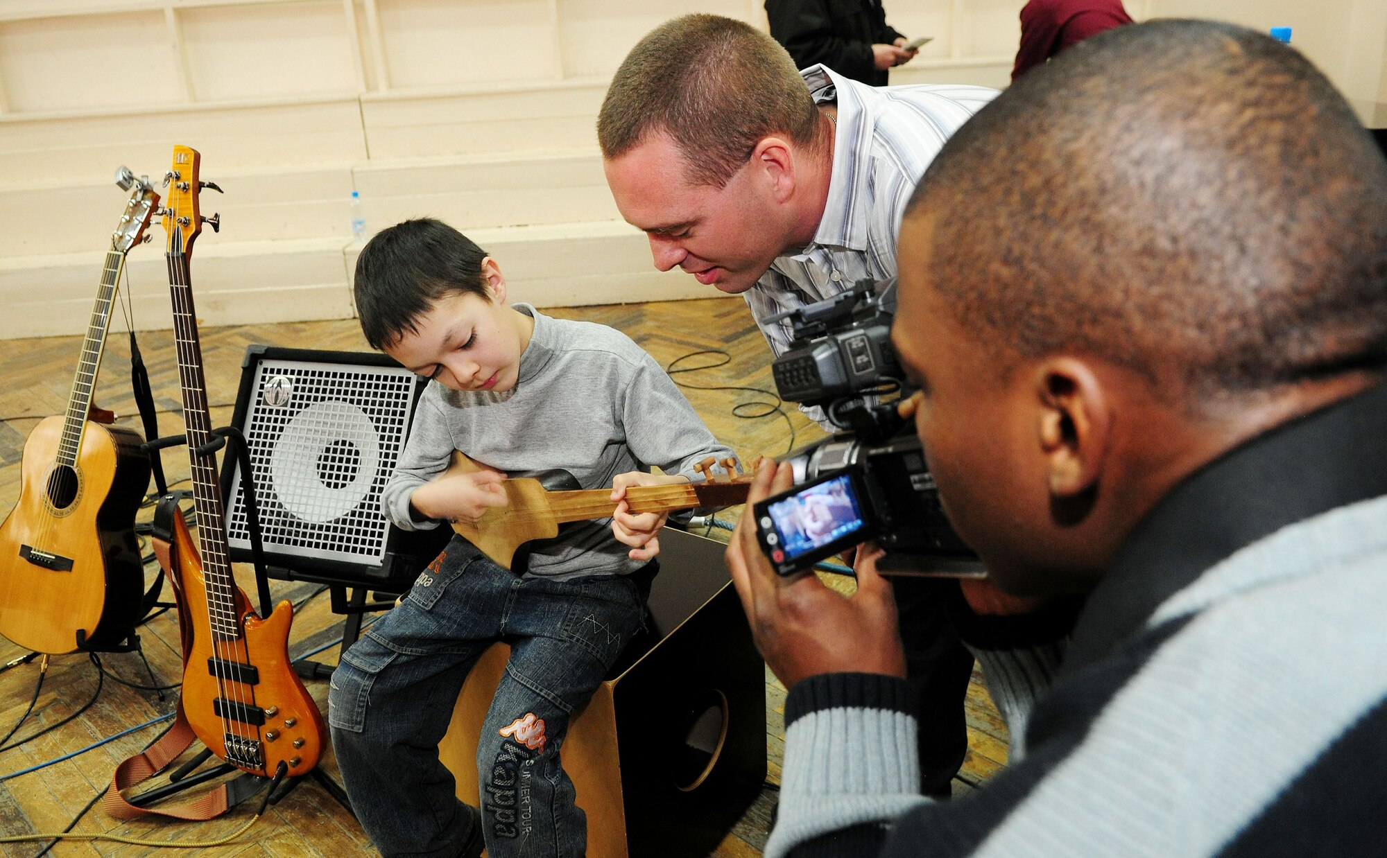 U.S. Air Force Senior Airman Isaac Garden, 376th Air Expeditionary Wing Public Affairs broadcaster, captures footage of Master Sgt. Eric Sullivan, "Celtic Aire" vocalist, bass, and cajon player, watching a young student play the Komuz after a performance at the Shubin Music School in Bishkek, Kyrgyzstan, Feb. 1, 2010. The U.S. Air Forces Central Public Affairs band received a unique opportunity to perform for the local community. (U.S. Air Force photo/Senior Airman Nichelle Anderson/released)
