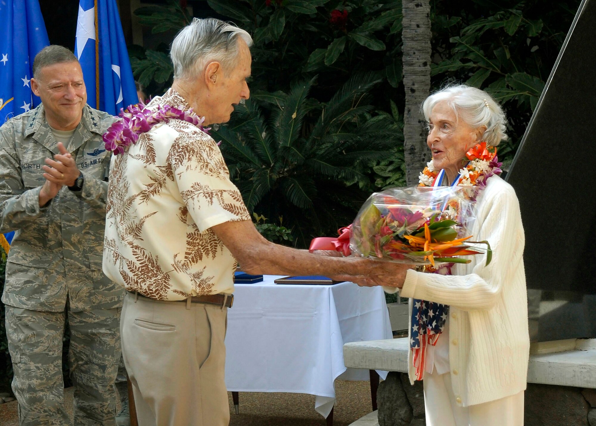 Col. (Ret.)  Alden Avery presents Mrs. Doris Avery (Dee) a member of the "Greatest Generation," with a bouquet of flowers at a medallion ceremony to honor her efforts in World War II, as Gen. Gary North, Pacific Air Forces commander, looks on. She received an Air Medal for her actions. In a ceremony to honor her, General North presented the Noncommissioned Officers' Association World War II Veterans Medallion to Mrs. Avery at the Courtyard of Heroes, Joint Base Pearl Harbor Hickam, Hawaii, Feb. 5, 2010, for her heroic efforts. Mrs. Avery served as a lieutenant in the Army Nurse Corps during World War II. As a flight nurse on medical air evacuation flights, Lieutenant Avery amassed more than 800 flight hours.   (U.S. Air Force photo/Tech. Sgt Jerome S. Tayborn)