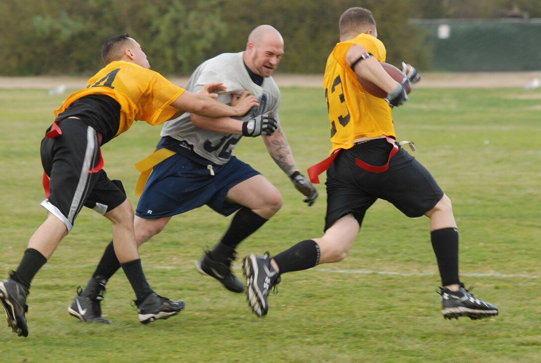Wide receiver Richard Harmon, right, trucks down the field with the ball while Coast Guard line backer Troy Fuller, center, struggles to stop him before being taken out by cornerback Steven Phillips, left, during the Commanding General's Cup Flag Football game at the depot sports field, Feb. 9. Both teams were undefeated going into the game, but Ceremonial prevailed as the best on the depot with a winning score of 26-7.