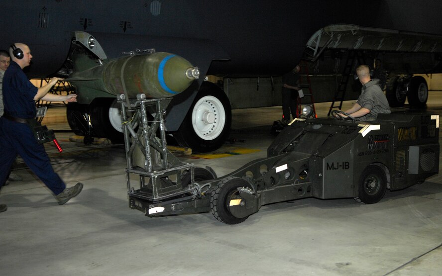 MINOT AIR FORCE BASE, N.D. -- Staff Sgt. Jason Eilo, 5th Aircraft Maintenance Squadron weapons load crew team member, walks along with a M-117 bomb as Airman 1st Class Kyle Herman, 5th AMXS weapons load crew member, drives the MJ1 jammer carrying the M-117 bomb to the B-52H Feb. 5. The load crew team is evaluated monthly on how quickly and precisely they can load weapons onto an aircraft. (U.S. Air Force photo by Airman 1st Class Ashley N. Avecilla) 