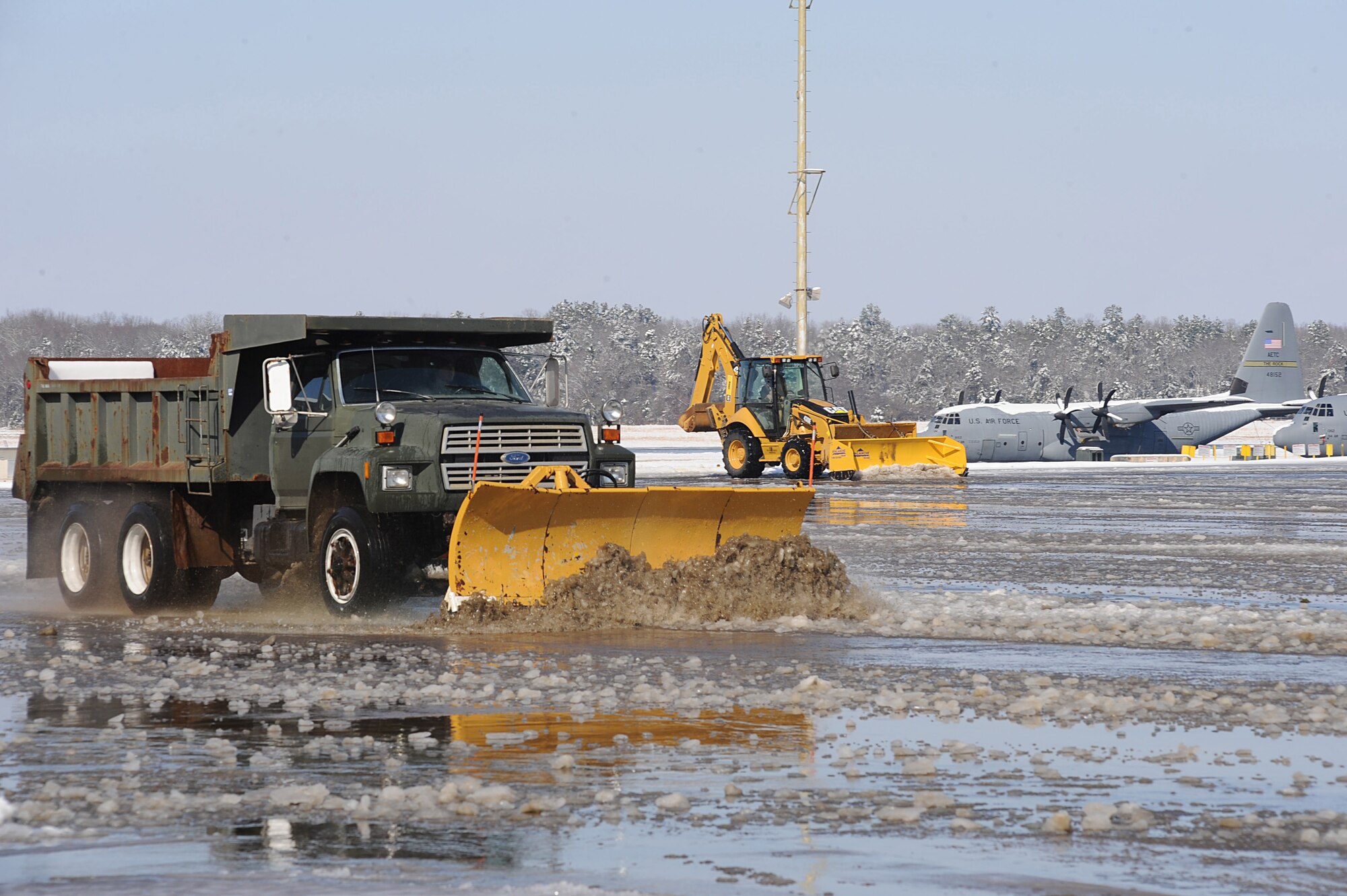 Staff Sgt. William Duqain, 19th Civil Engineer Squadron pavement and equipment operator, drives a 10-ton snow plow and civil service worker David Cole, 19th Civil Engineer Squadron heavy equipment operator, operates a Caterpillar backhoe pushing snow, ice and water Feb. 9 to clear the flightline for flying operations. Sergeant Duqain and Mr. Cole are preparing the base to resume normal operations by pushing mass quantities of snow and ice that had fallen during a winter storm Feb. 8 from the flightline, roads and parking lots.  (U.S. Air Force photo by Staff Sgt. Chad Chisholm)
