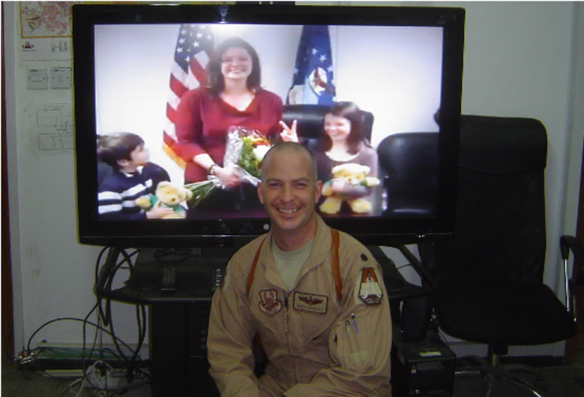 Lt. Col. Russel Driggers kneels in front of the video teleconference monitor in Iraq during his promotion ceremony.  His children, Emma and Leo, and wife Janet were able to join in the ceremony via VTC.  Colonel Driggers had his new rank pinned on by the Iraqi Air Force Director of Air and Space Operations and the Iraqi Air Operations Center Military Training Team Chief. (USAFE Photo)