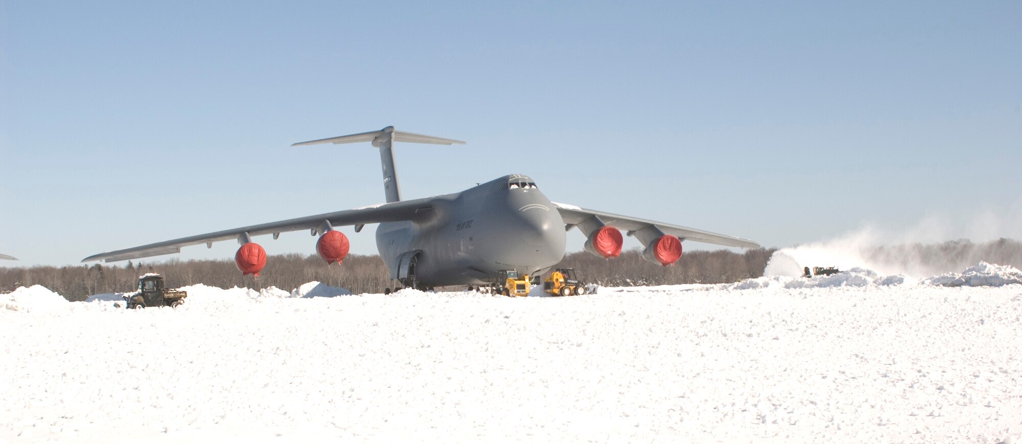 Crews work to remove snow from around a C-5 Galaxy at Dover Air Force Base Feb. 8.  The aircraft is undergoing the Avionics Modernization Program and did not depart with the rest of the aircraft from Dover.  Dover  launched most of the aircraft to clear the flightline for snow removal efforts.  (U.S. Air Force photo/1st Lt. Brian Maguire)