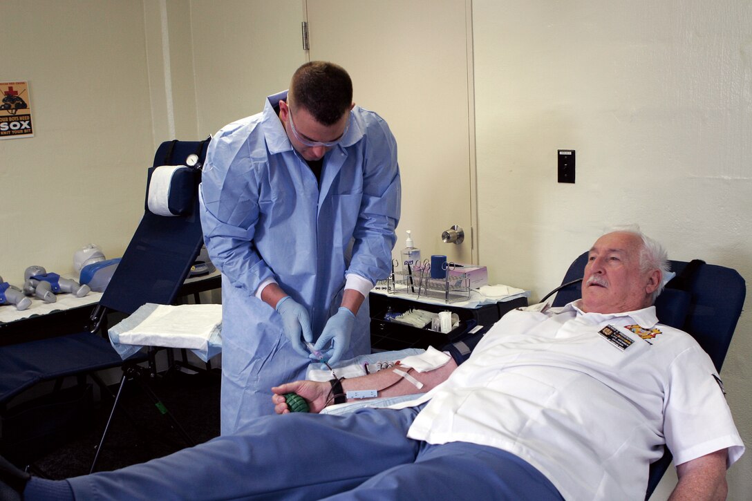 Petty Officer 3rd Class Jason Shrunk, a corpsman with the Armed Services Blood Bank Center, observes the blood donation of retired Air Force Staff Sgt. Dennis Provencher.