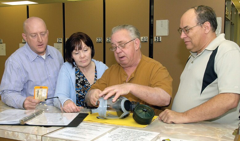 Quality assurance evaluators with the 72nd Logistics Readiness Squadron’s Supply Quality Flight watch warehouse specialist Tom Thomas demonstrate a gas mask inspection that’s performed on a random sampling every six months. QAEs from left are George Eastling, Candy McDonald and John Sullivan.  (Air Force photo by Margo Wright)