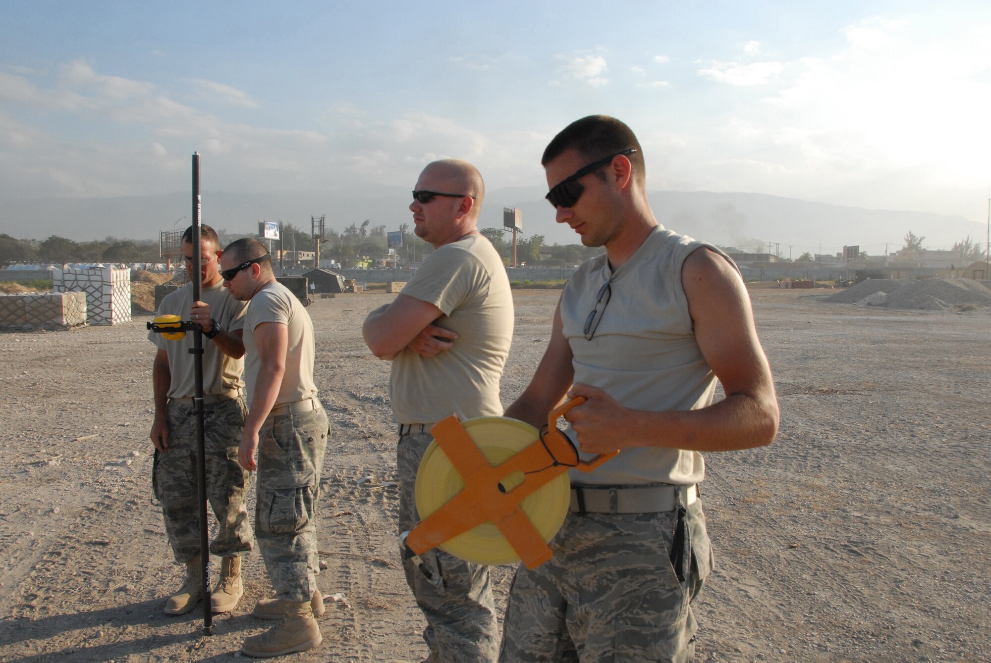 Senior Airman Kristopher P. Stewart (center), and Engineering Assistant with the 190th Air Refueling Wing, Topeka, Ks., rolls a tape measure while working with other members of the Air Force to survey the Port- au-Prince airport.  Stewart is one of 46 members of the Kansas Air National Guard that deployed to Haiti to build support infrastructure, including an Expiditionary Medical Support (EMEDS) support hospital.