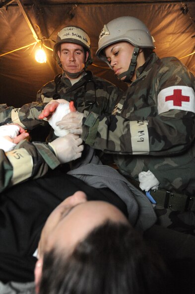 MINOT AIR FORCE BASE, N.D. -- Capt. Brian Withers, 5th Medical Operations Squadron chief of medical services, and Senior Airman Rhianna Scott, 5th Medical Operations Squadron medical technician dress two simulated gunshots wound on the hands of Airman Jeanine Gregory, 5th Communications Squadron knowledge operations manager, a moulage victim suffering from as part of Prairie Knight 10-1 here Feb. 9. Prairie Knight 10-1 is an exercise geared to prepare the 5th Bomb Wing Warbirds for a conventional warfare environment. (U.S. Air Force photo by Senior Airman Jesse Lopez)