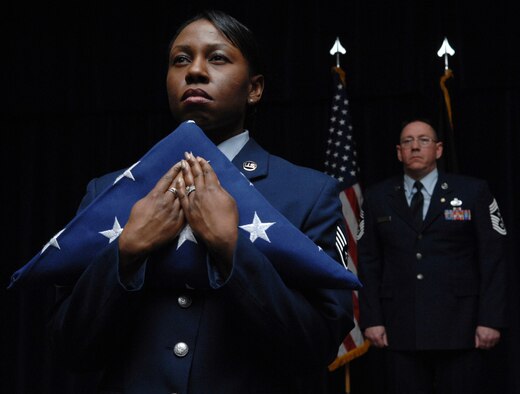 SPANGDAHLEM AIR BASE, Germany -- Staff Sgt. Marcie Ireland, 52nd Force Support Squadron lodging supervisor, holds the flag as retired Chief Master Sgt. Bruce Kenney, former 52nd Fighter Wing command chief, watches during the "Progression of Ranks" portion of his retirement ceremony Feb. 11 at Club Eifel. Chief Kenney served in the Air Force for 30 years. (U.S. Air Force photo/Airman 1st Class Nick Wilson)