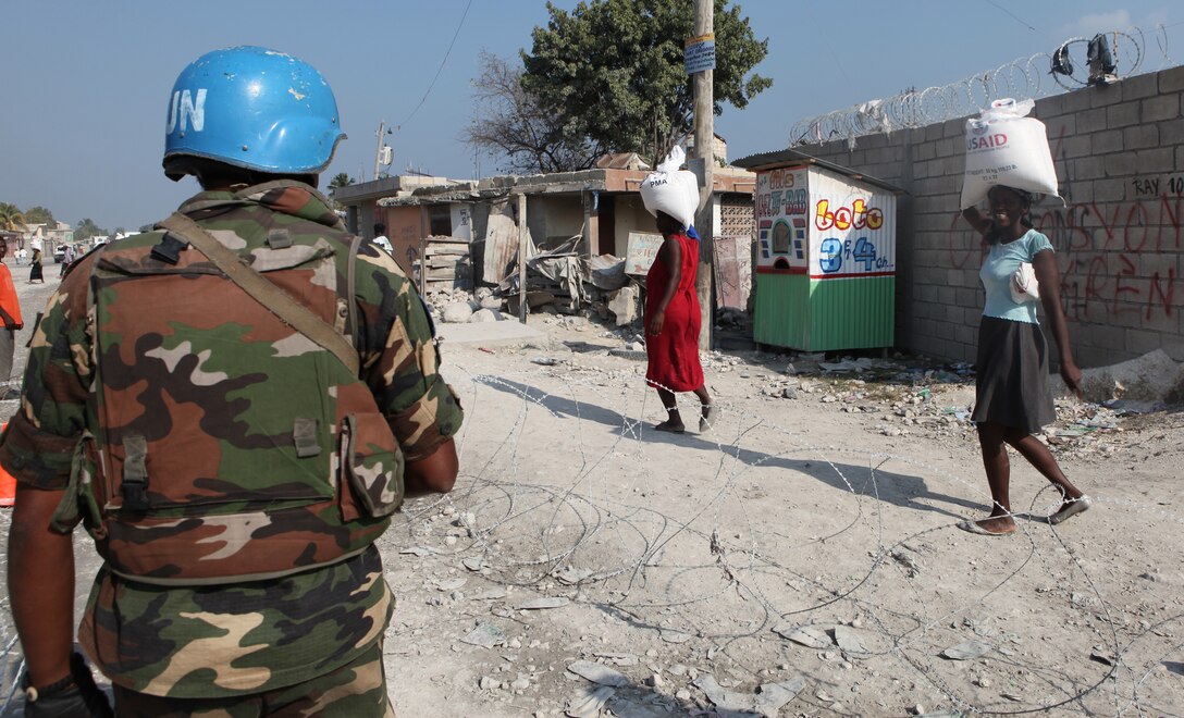 A United Nations worker observes local Haitian women carry bags of humanitarian aid rations during a humanitarian aid distribution in Carrefour, Haiti, Feb. 12, 2010. Marines of Battalion Landing Team, 3rd Battalion, 2nd Marine Regiment, 22nd Marine Expeditionary Unit, provided security for a local non-government organization as they supplied local Haitians with 50 pound bags of rice.