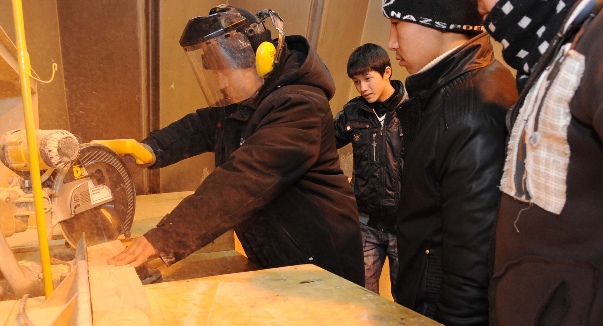 A 376th Expeditionary Civil Engineer Squadron contractor shows Jeni Jehr Vocational School students from Kyrgyzstan how to safely use a miter saw during their tour of the Transit Center at Manas Feb. 13. These students were touring the 376th ECES to see how Airmen conduct military operations here and learn different civil engineer techniques. (U.S. Air Force photo/Senior Airman Nichelle Anderson/released)