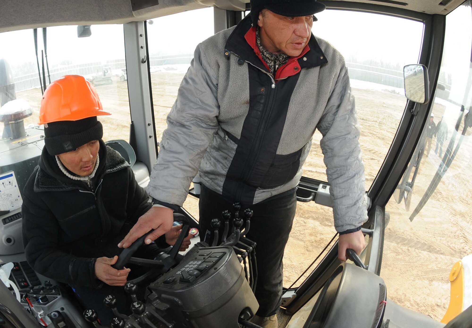 Andre Ivanan, 376th Expeditionary Civil Engineer Squadron contractor, shows Holdar Farhudinov, a student from the Jeni Jehr Vocational School, Kyrgyzstan, how to drive a bull dozer at the new construction area of the Transit Center at Manas Feb. 13. Twenty students visited the installation to see how Airmen conduct military operations here and learn different civil engineer techniques. (U.S. Air Force photo/Senior Airman Nichelle Anderson/released)