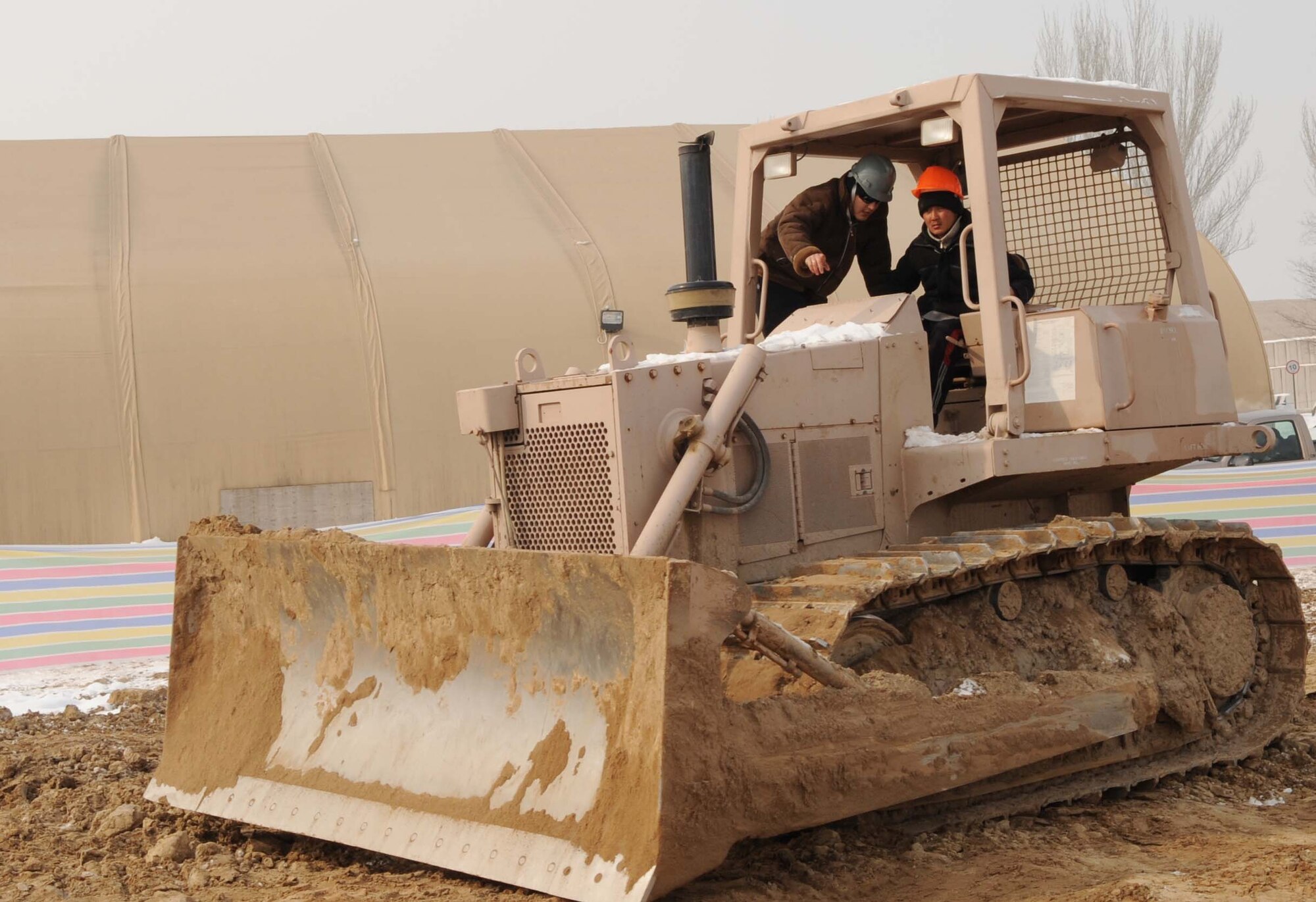 Davran Sadykova, 376th Expeditionary Civil Engineer Squadron contractor, shows Holdar Farhudinov, a student from the Jeni Jehr Vocational School, Kyrgyzstan, how to drive a bull dozer at the new construction area of the Transit Center at Manas Feb. 13. Twenty students visited the installation to see how Airmen conduct military operations here and learn different civil engineer techniques. (U.S. Air Force photo/Senior Airman Nichelle Anderson/released)