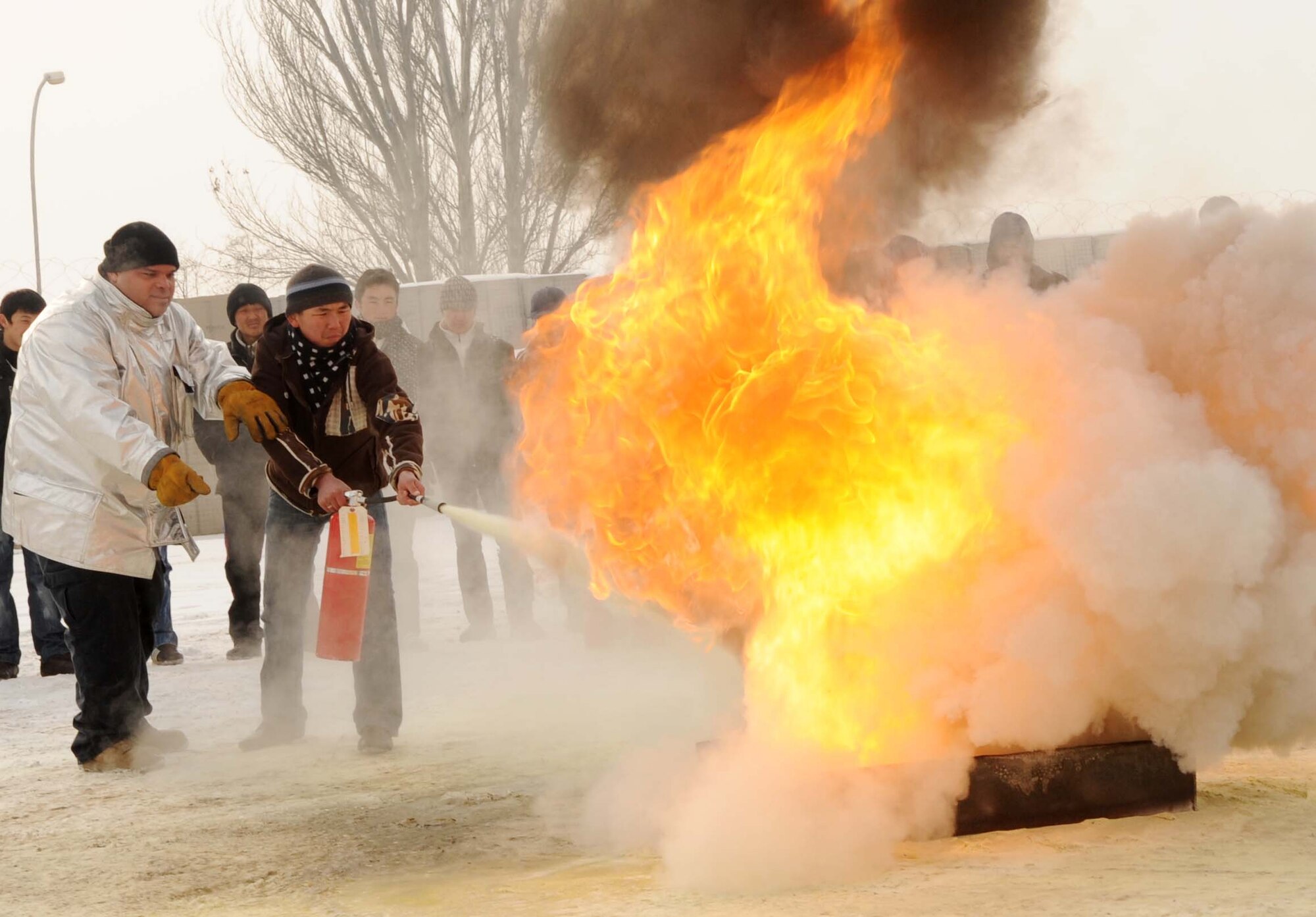 376th Expeditionary Civil Engineer Squadron fire fighter, Jay Morris, and Jeni Jehr Vocational School student, Serik Kamchibekov, put out a controlled burn during fire extinguisher training Feb. 13. These students were touring the 376th ECES at the Transit Center at Manas, Kyrgyzstan, to see how Airmen conduct military operations here and learn different civil engineer techniques. (U.S. Air Force photo/Senior Airman Nichelle Anderson/released)