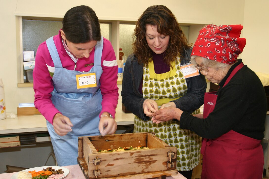 Kikuko Shinjo, caretaker at the Iwakuni Youth Hostel, assists Laura Reed (right) and Marcy Pearson (left) in showing the class how to make Iwakuni Sushi Feb. 16.