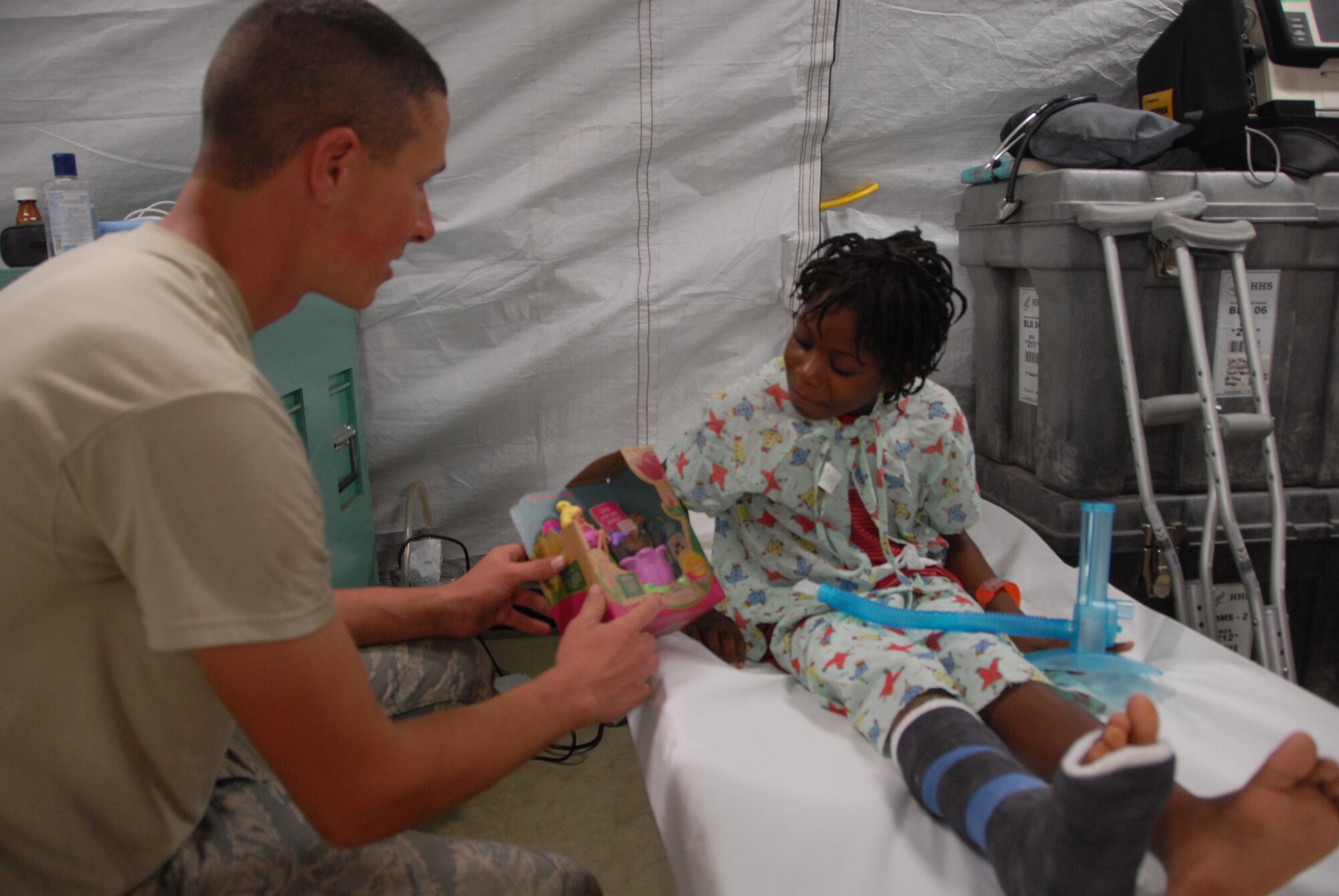Senior Airman Matt Greene gives a doll to Murielle, an earthquake survivor being treated in EMEDS, which the 190th Civil Engineers constructed a few days earlier.