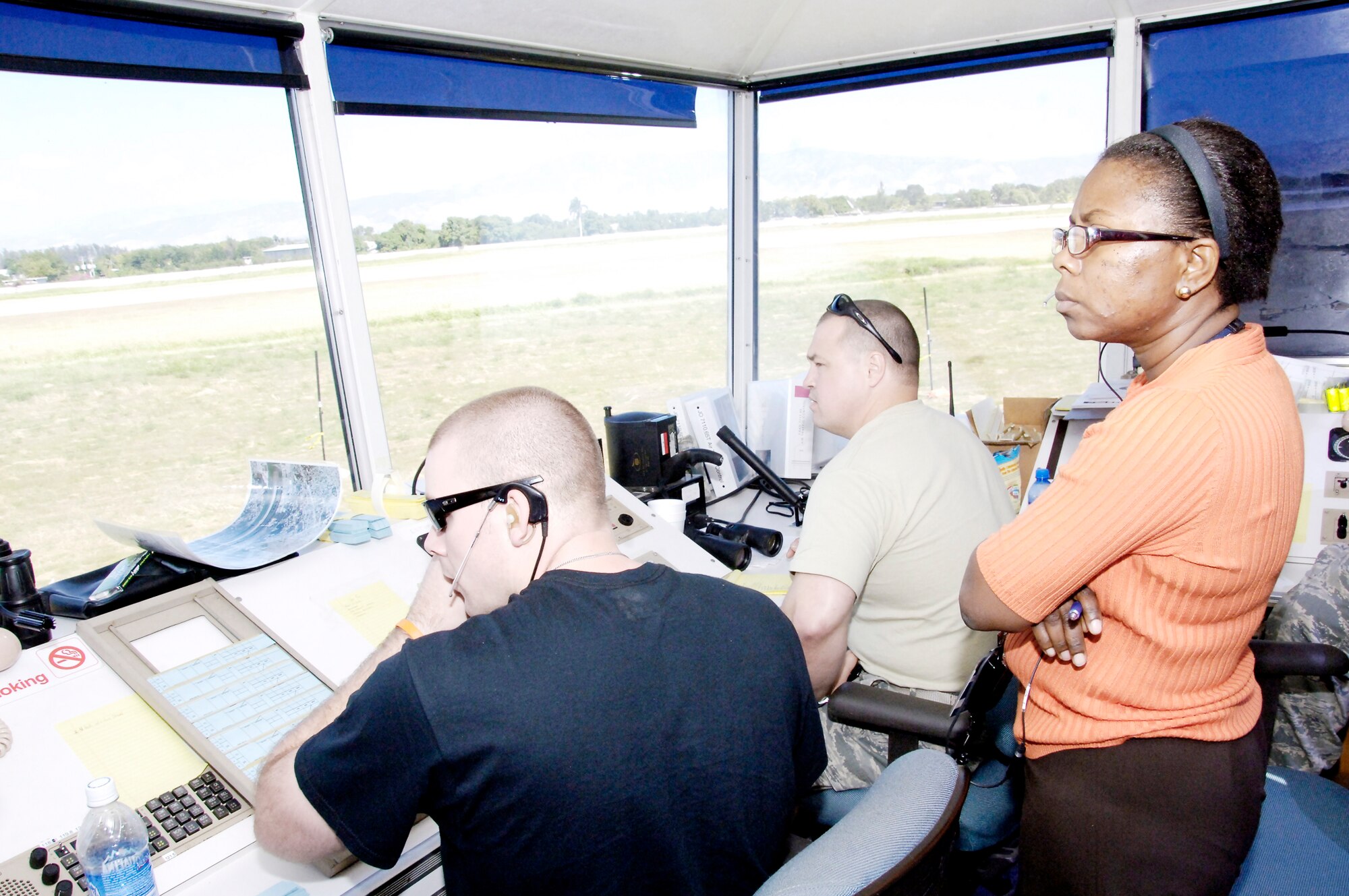 Nadia Adma observes tower operations from Tech. Sgt. Robert Stewart (left) and Tech. Sgt. Jerry Scurlock (right) Feb. 2, 2010, at the airport in Port-au-Prince, Haiti. Haitian controllers will observe the Air Force controllers for two weeks and then the Haitian controllers will run the tower with the Air Force as advisers until they feel comfortable taking over flight responsibilities. Ms. Adma is a Haitian air traffic controller. Sergeants Stewart is assigned to the 260th Air Traffic Control Squadron. Sergeant Scurlock is assigned to the 258th ATCS. (U.S. Air Force photo/Tech. Sgt. Larry W. Carpenter Jr.) 