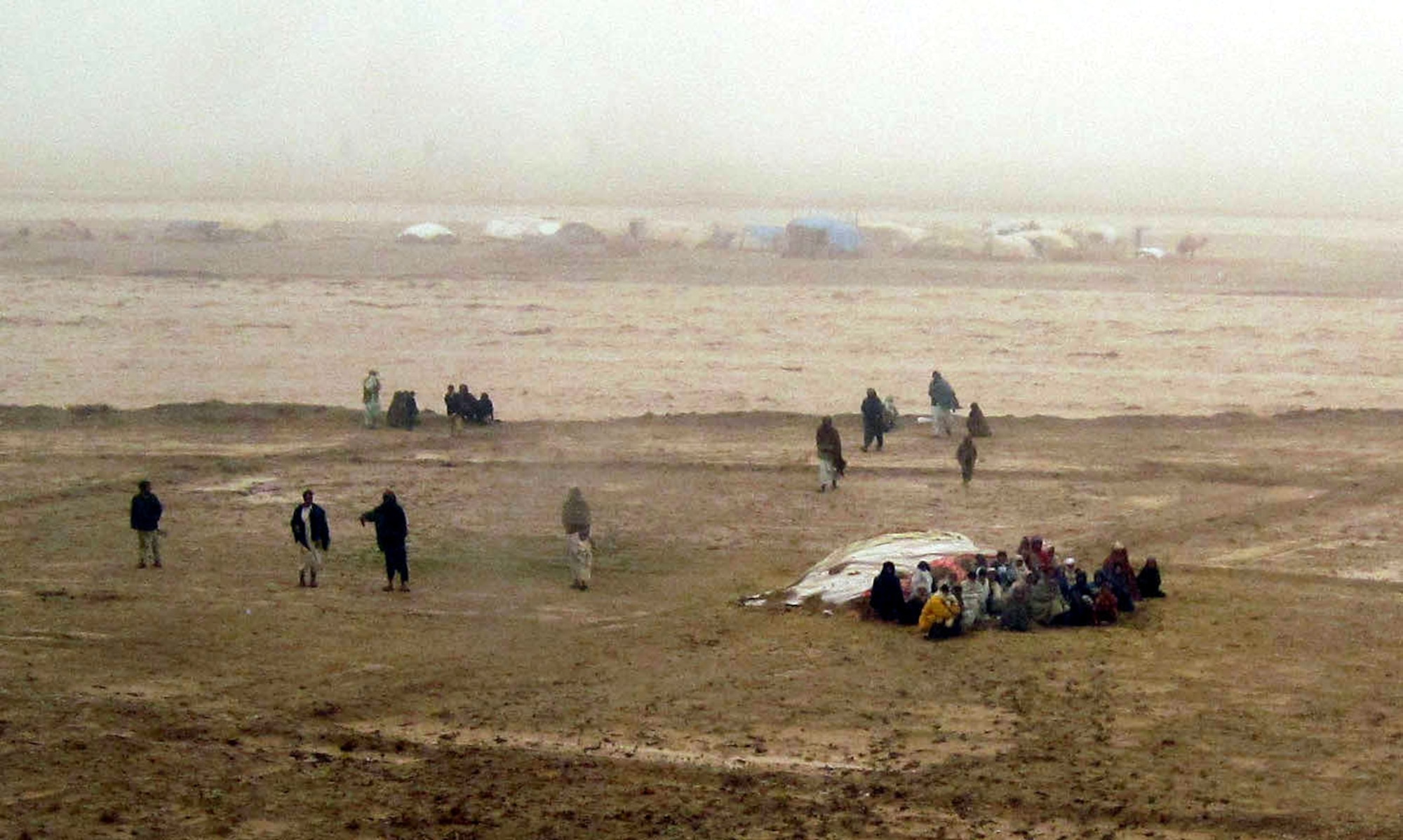 Afghan members of the nomadic Kuchi tribe gather to look at the island that was created as rising, torrential flood waters closed in on their village, cutting them off from any escape Feb. 8, 2010. Afghan National Army Air Corps servicemembers and their U.S. Air Force advisors airlifted the Afghans to the other side of the river where they were safe on higher ground. (U.S. Air Force photo by Capt. Tyler Rennell/Released) 
