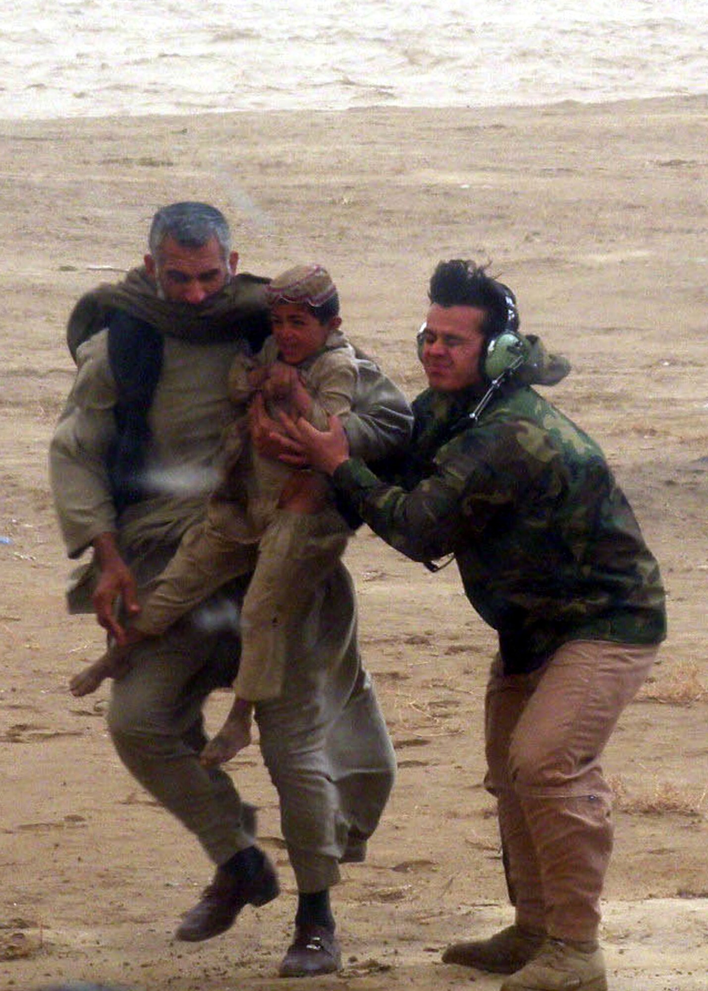 An Afghan National Army Air Corps servicemember helps a man of the nomadic Kuchi tribe carry his frightened child aboard a helicopter for an airlift to safety as their village is nearly overtaken by a flash flood Feb. 8, 2010.  (U.S. Air Force photo by Lt. Col. Prejean/Released)