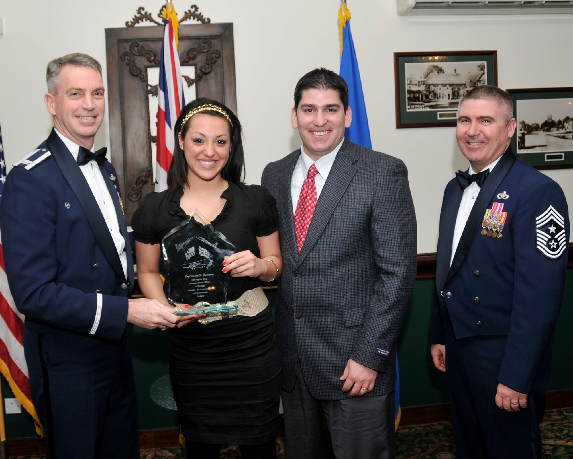 Col. Lawrence Reed, 48th Fighter Wing vice commander (left) and Chief Master Sgt. James Lucas present Rick and Melissa Enriquez, husband and daughter of Capt. Taona A. Enriquez, 748th Aircraft Maintenance Squadron, with the award for Field Grade Officer of the Year at the annual awards at the Eagles Landing Feb 13. (U.S. Air Force photo by Airman 1st Class Eboni Knox)