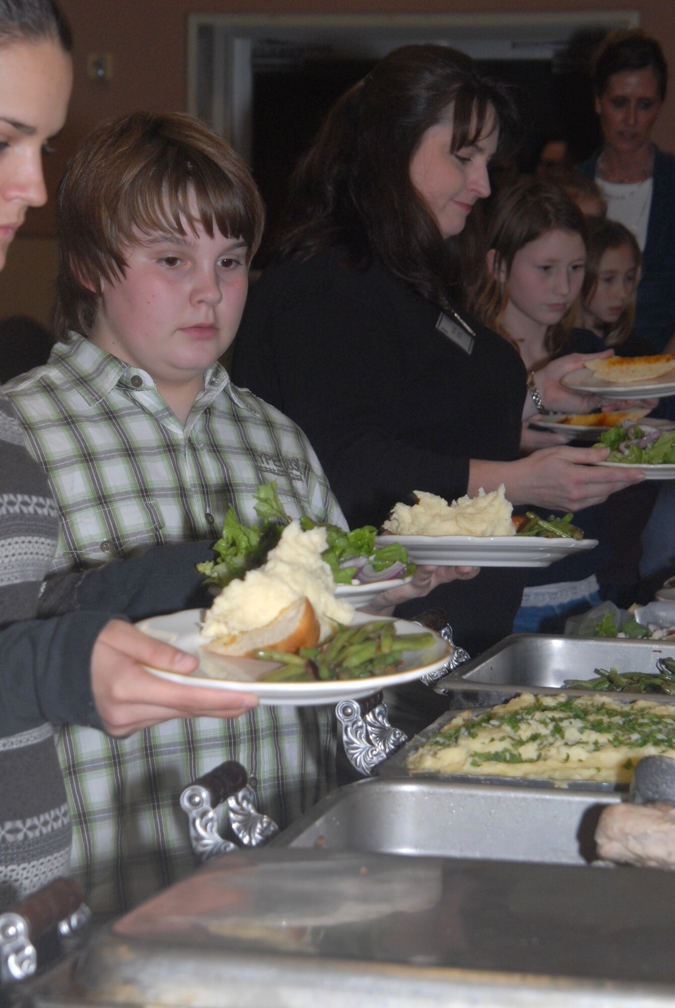 Goodfellow spouses and their children get a serving of the food prepared by Chef Jason Helfer, Peasant Village Restaurant, San Angelo, during the Key Spouses dinner Thursday night at the Event Center ( U.S. Air Force photo by Airman 1st Class Anne Gathua)